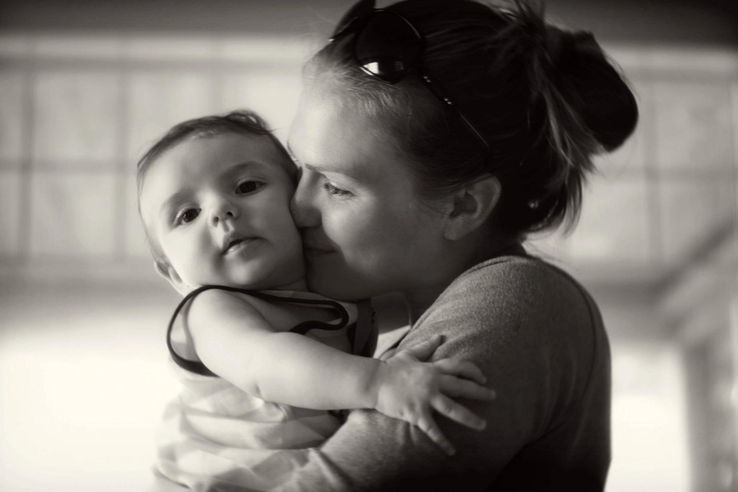 Mother kissing baby on cheek in tender black and white portrait photo.