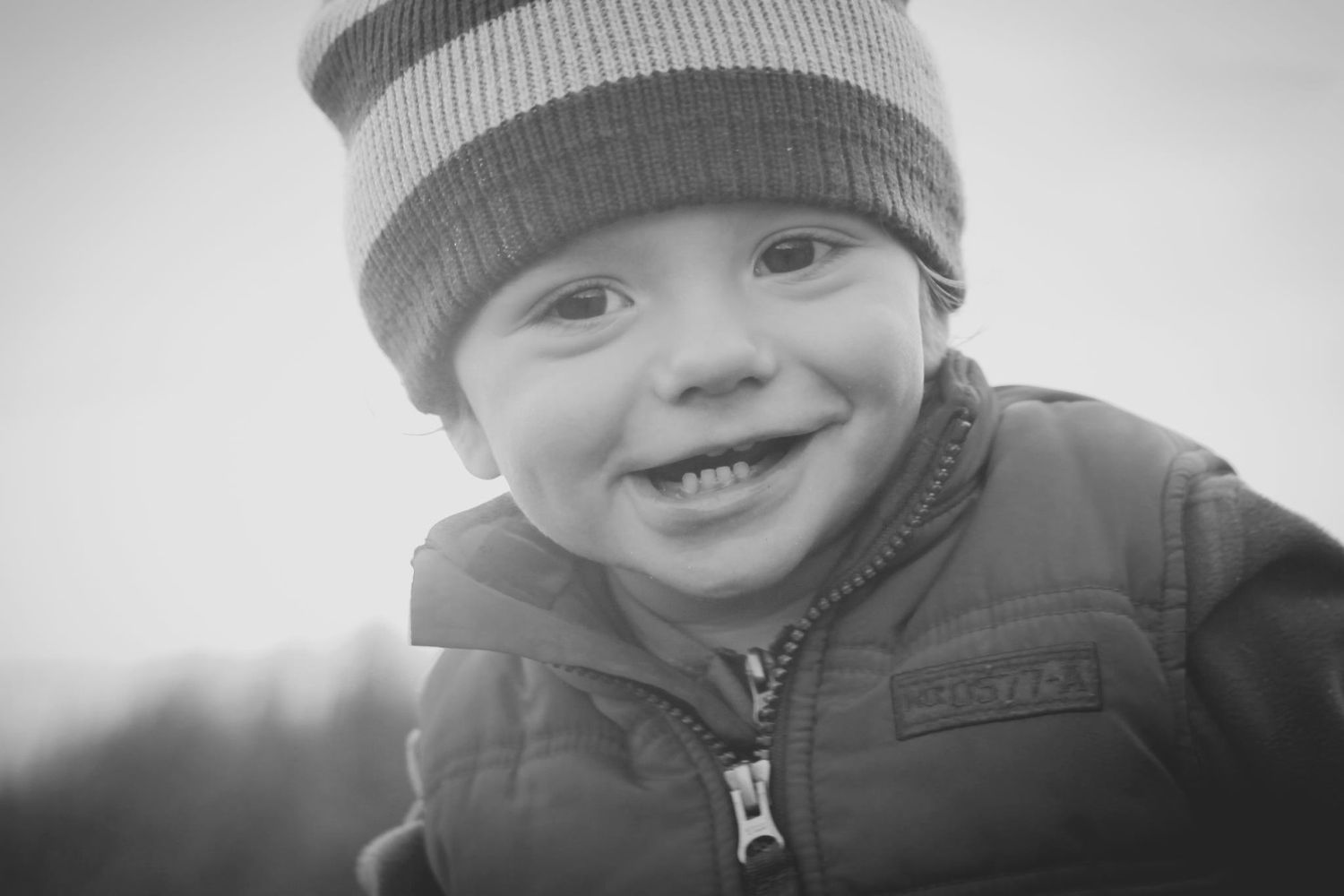 Happy smiling toddler boy wearing striped winter hat and jacket in black and white photo.