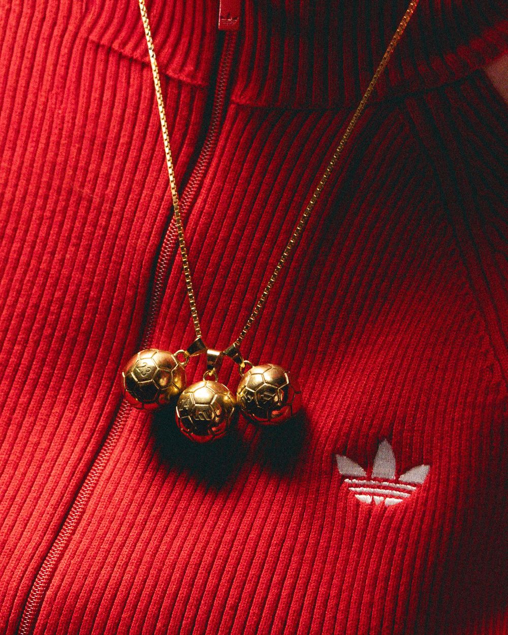 Gold pendant necklace with black beads photographed against vibrant red corduroy fabric background.