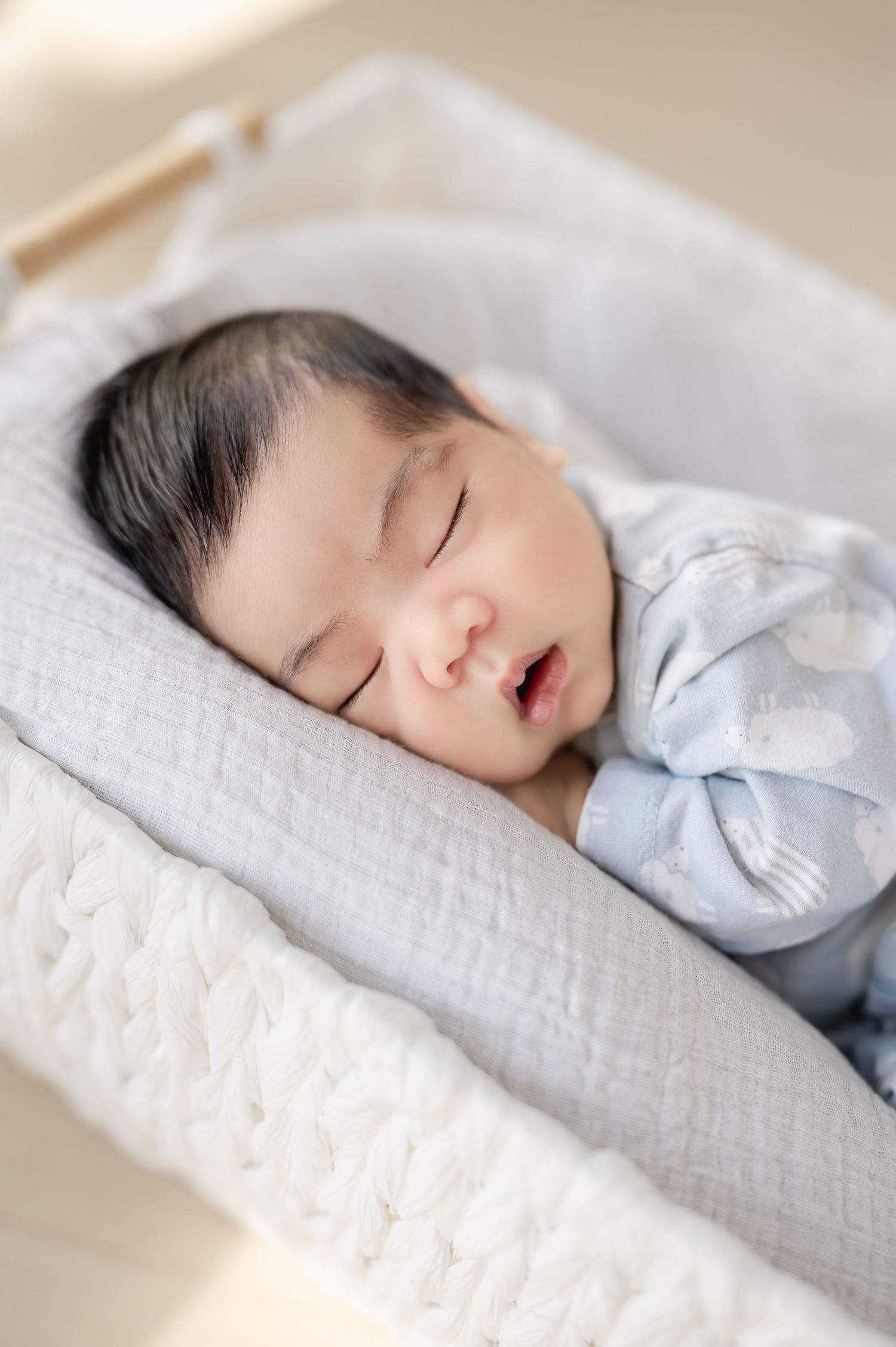 A sleeping baby lies peacefully on white bedding wearing light blue clothing.
