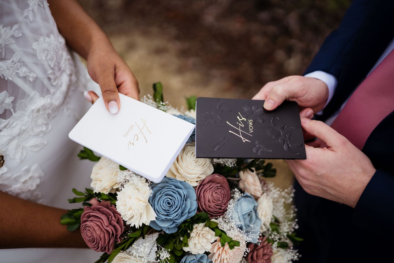 Wedding ceremony details with hands holding a card next to elegant floral arrangements featuring white and dusty blue roses.