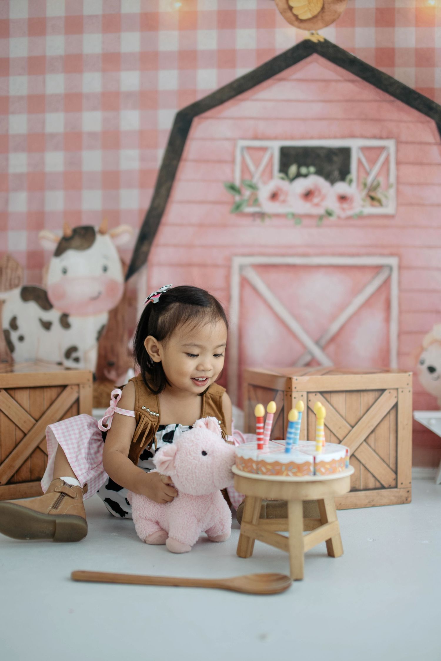 A farm-themed birthday setup with a pink barn backdrop, wooden furniture, and stuffed animal decorations.