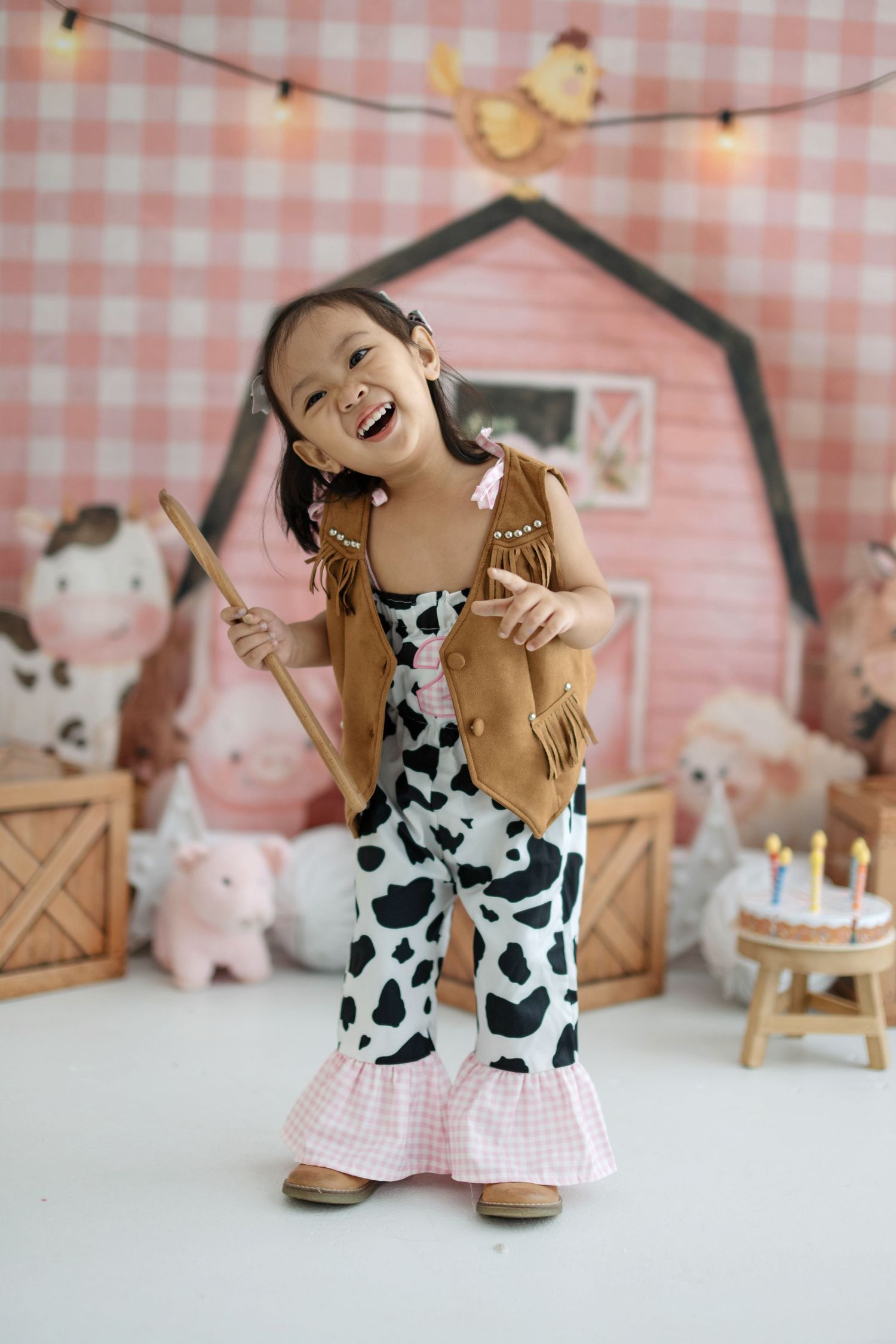 A playful birthday photo shoot setup with a pink gingham backdrop, string lights, and farmhouse decor.