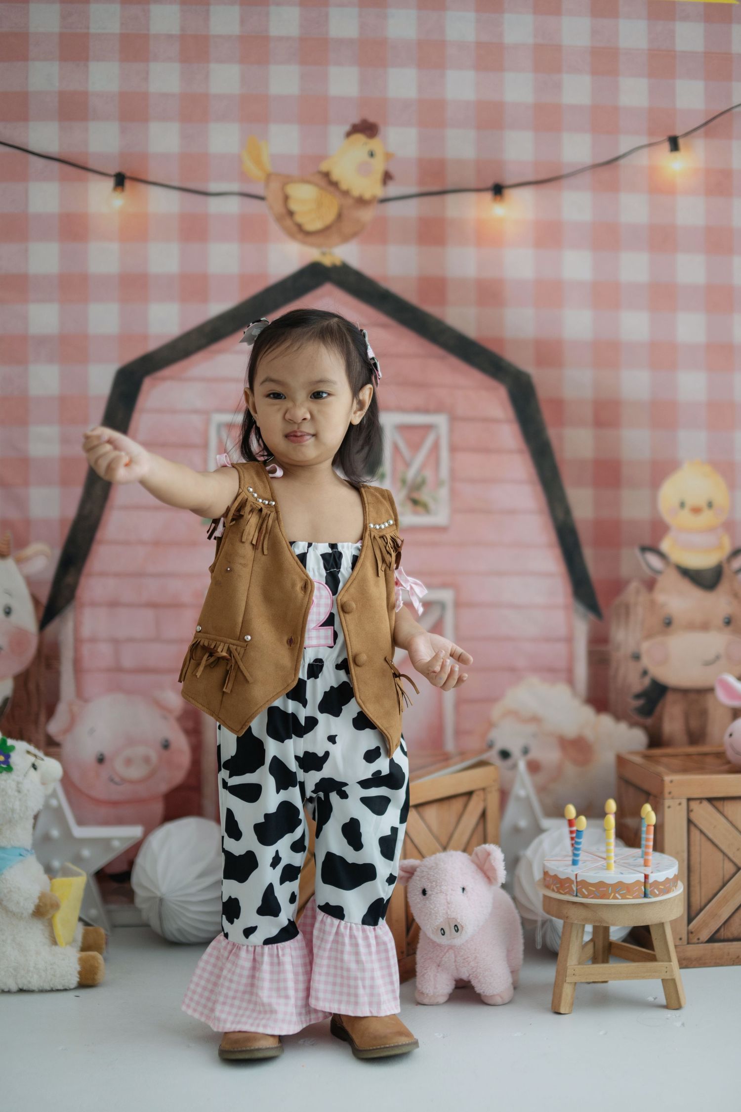 A barnyard-themed birthday party setup with cow print, wooden accents, and pink gingham background.