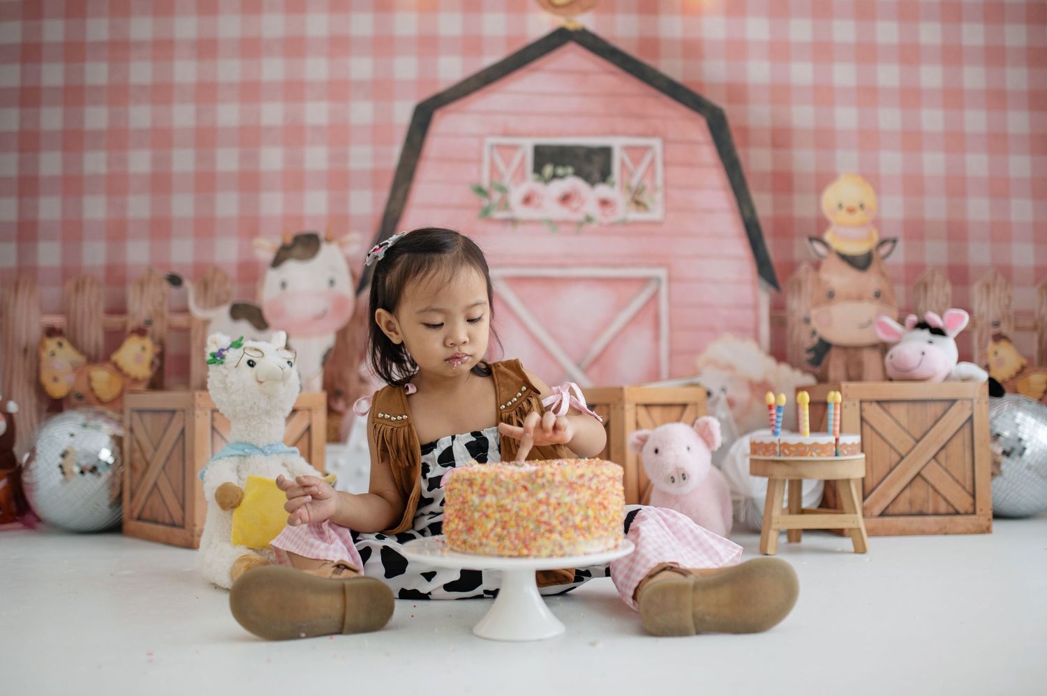Pink gingham backdrop with rustic barn doors and farm animal decorations creates a charming barnyard party setting.