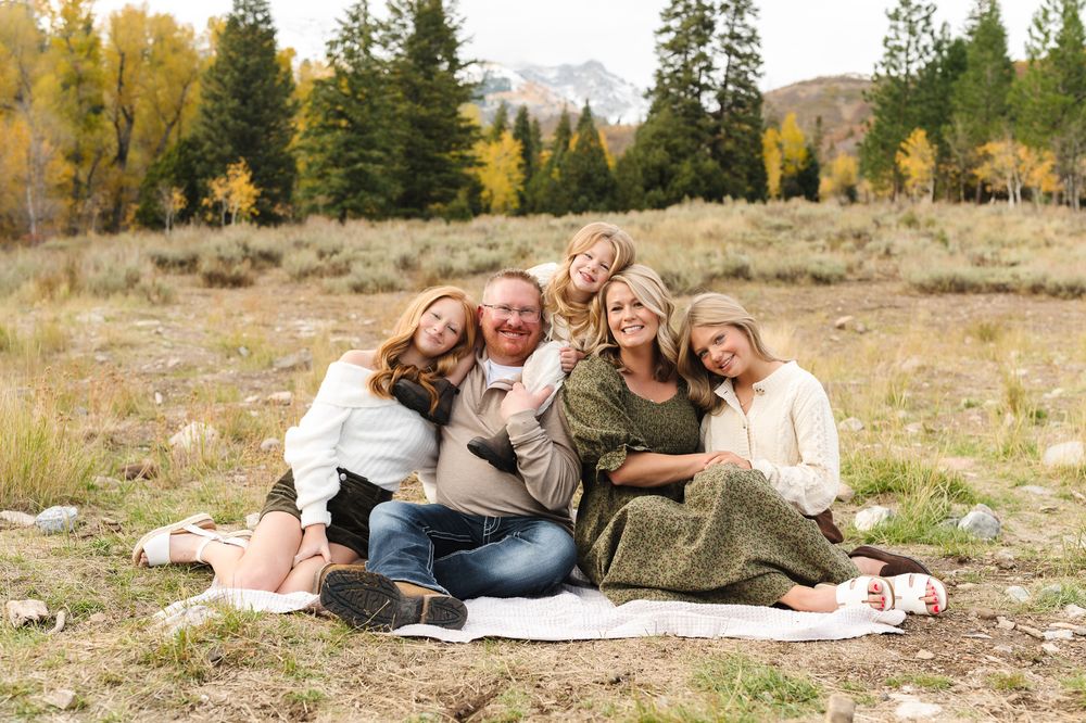 A Family laying on blanket in autumn mountain meadow with evergreen trees and golden aspens in background in American Fork Canyon.