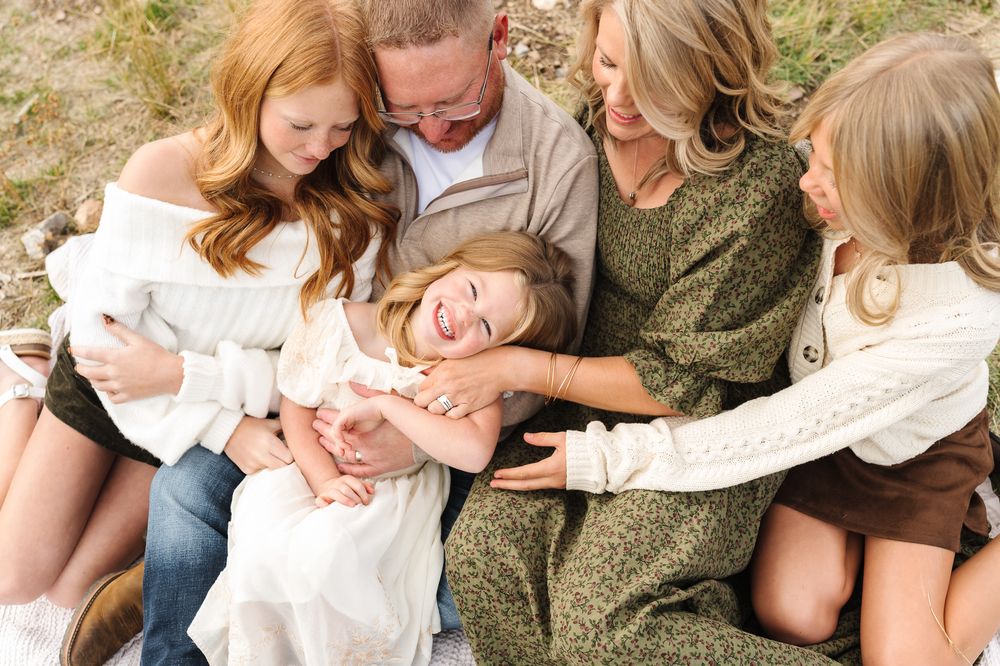 A family sits together on grass sharing tender moments in a series of candid outdoor photographs.