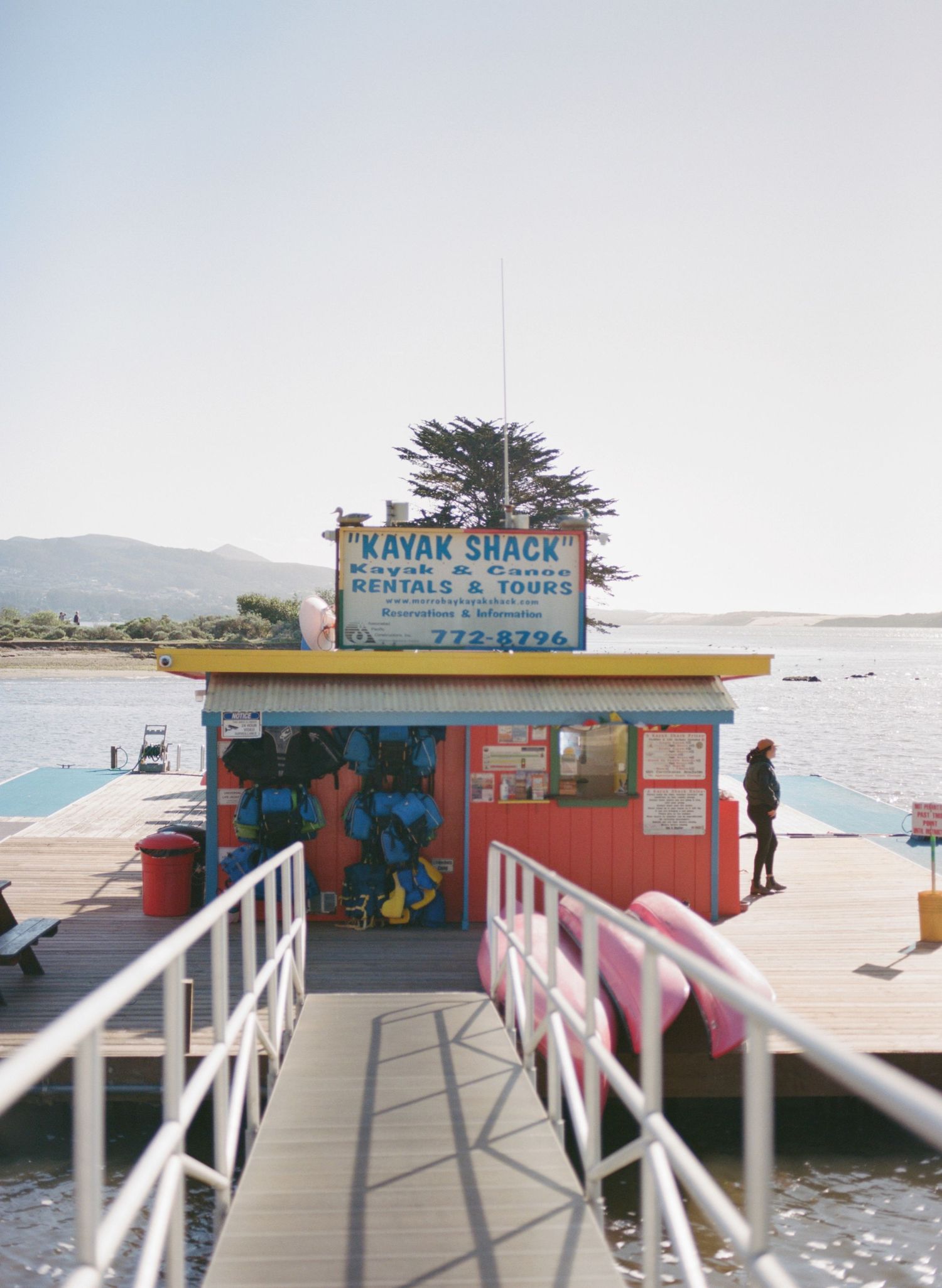 Kayak rental shack on a wooden pier overlooking calm waters with mountains in the background.