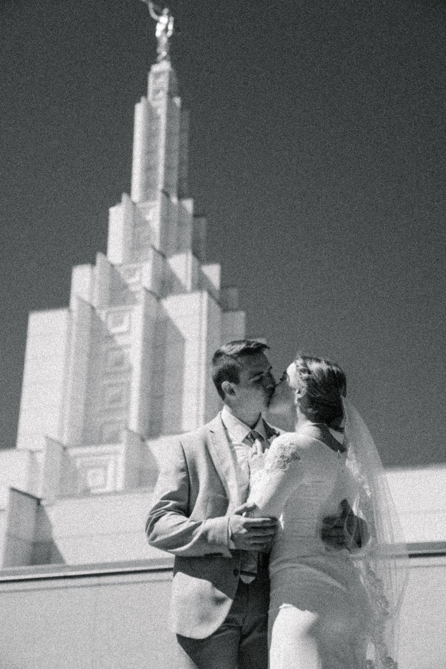 Black and white portrait of a bride and groom standing in front of a temple during their wedding day.