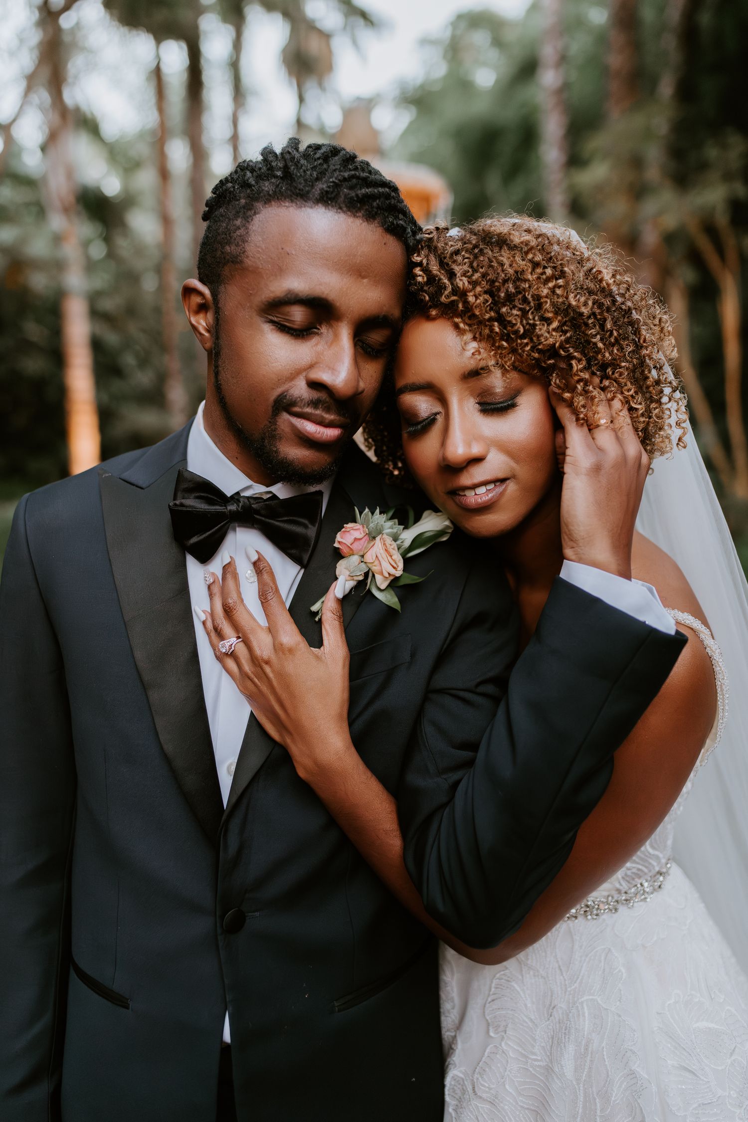 Elegant bride and groom share a tender embrace in a lush outdoor wedding portrait.