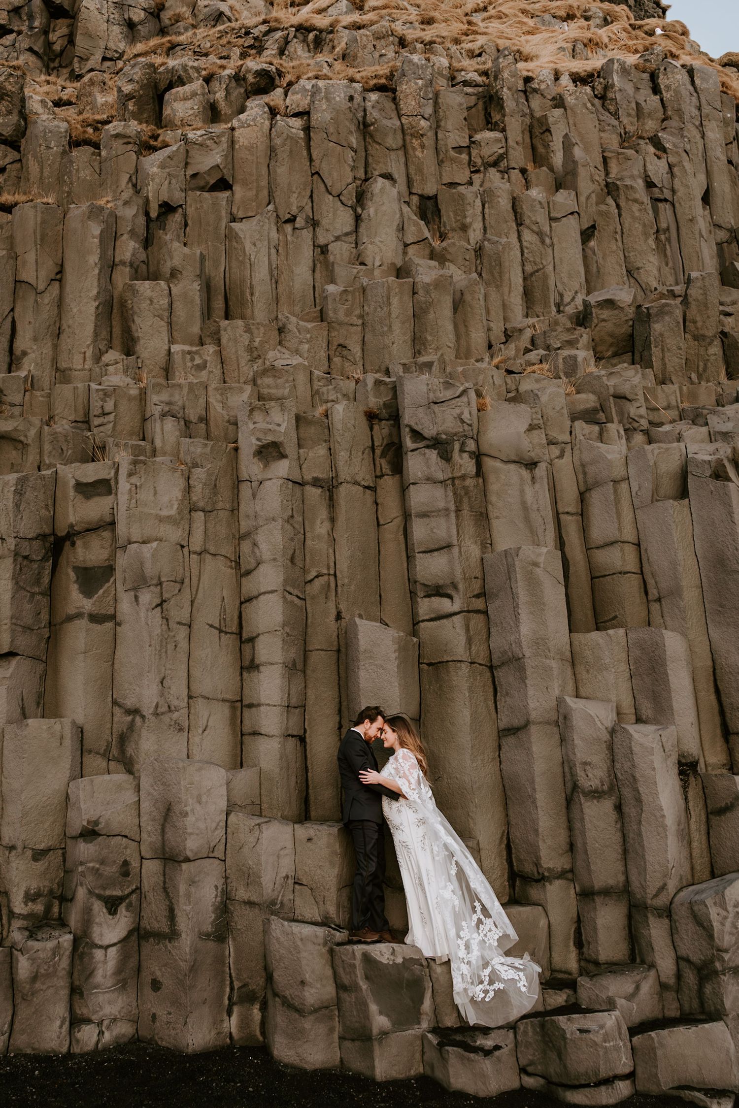 Bride and groom sharing a romantic moment against dramatic basalt column rock formations.