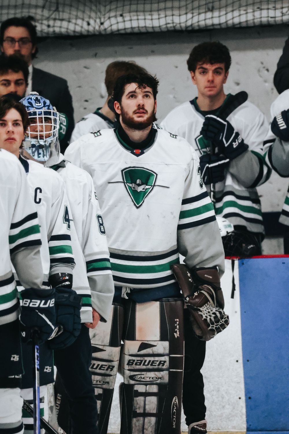 Hockey team wearing white jerseys with green stripes lined up on bench.