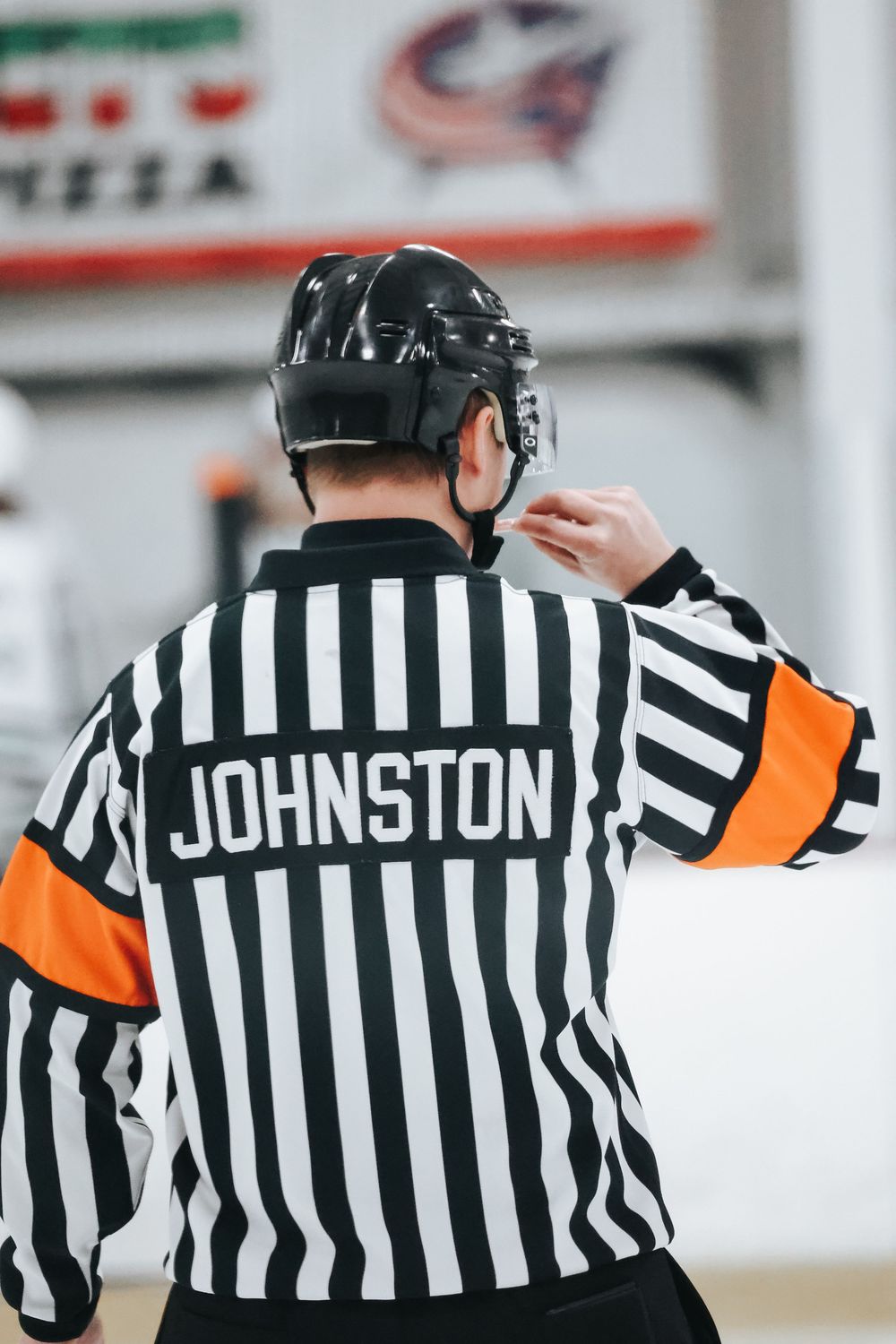 Row of hockey referees in traditional black and white striped uniforms shown from behind.