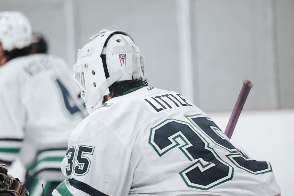 Hockey players in white jerseys with numbers visible during team practice.