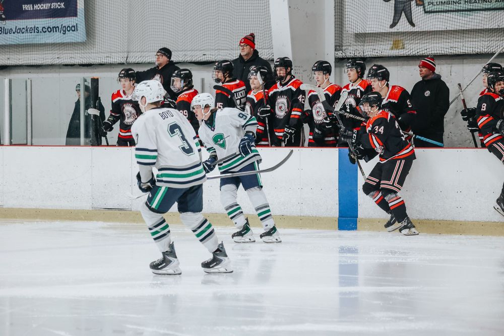 Hockey players in white and green jerseys skate on ice during an intense game against opponents in red and black.