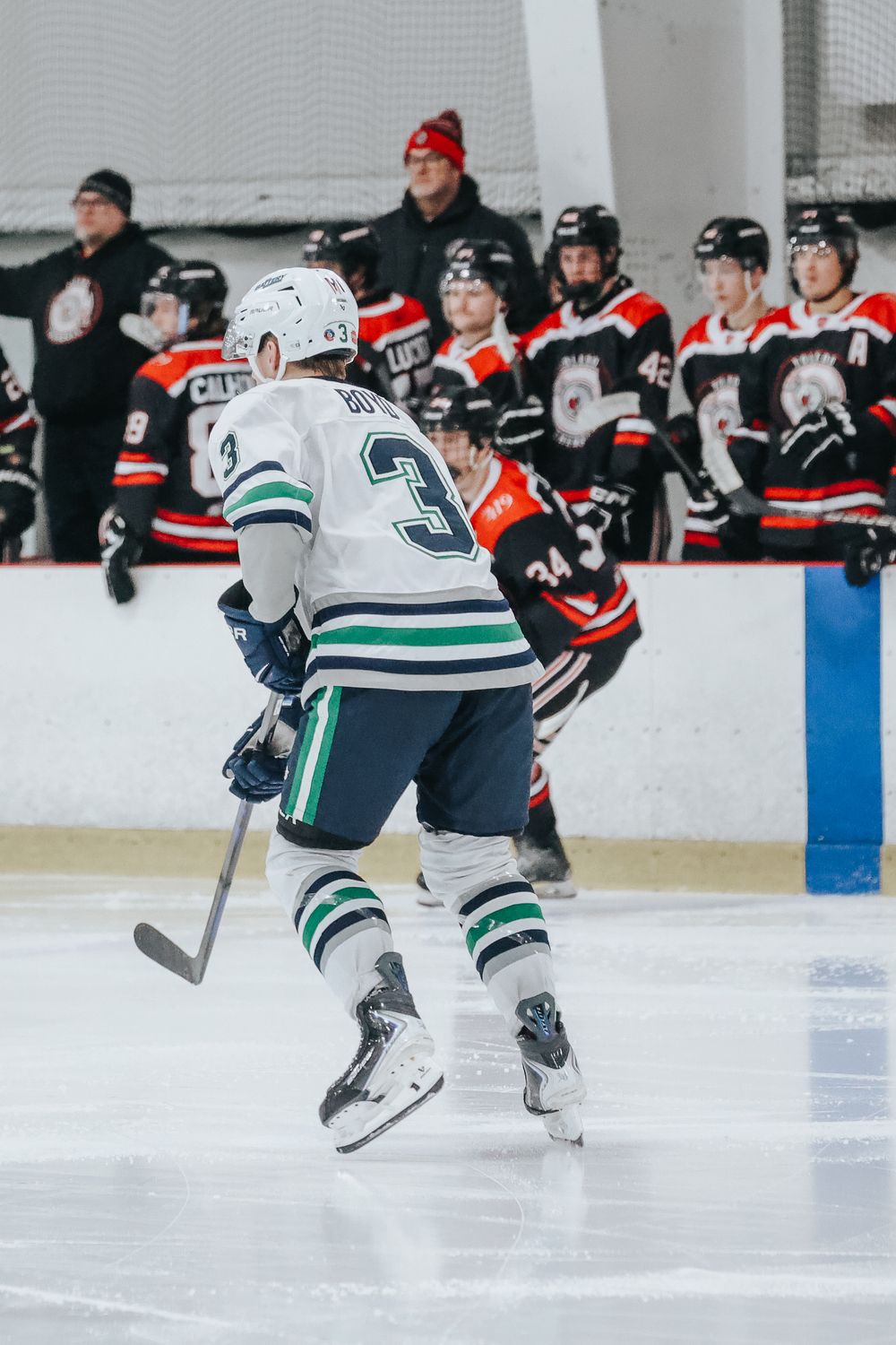 Hockey players in white and green uniforms skate swiftly across the ice during a competitive match.