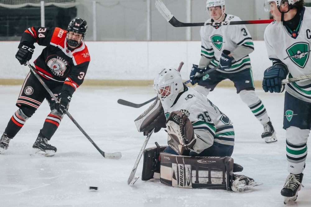 Hockey players from opposing teams compete for the puck near the goal crease during gameplay.