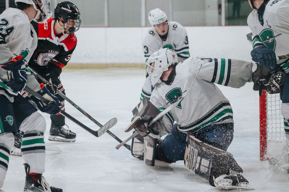 Players scramble for position around the goal net during an intense hockey game sequence.