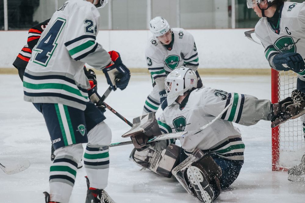 Hockey players crowd around the goal area during a competitive game situation.