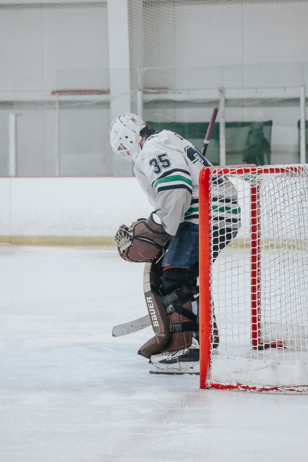 Goalie in white and green uniform defends the red goal post during a hockey match.