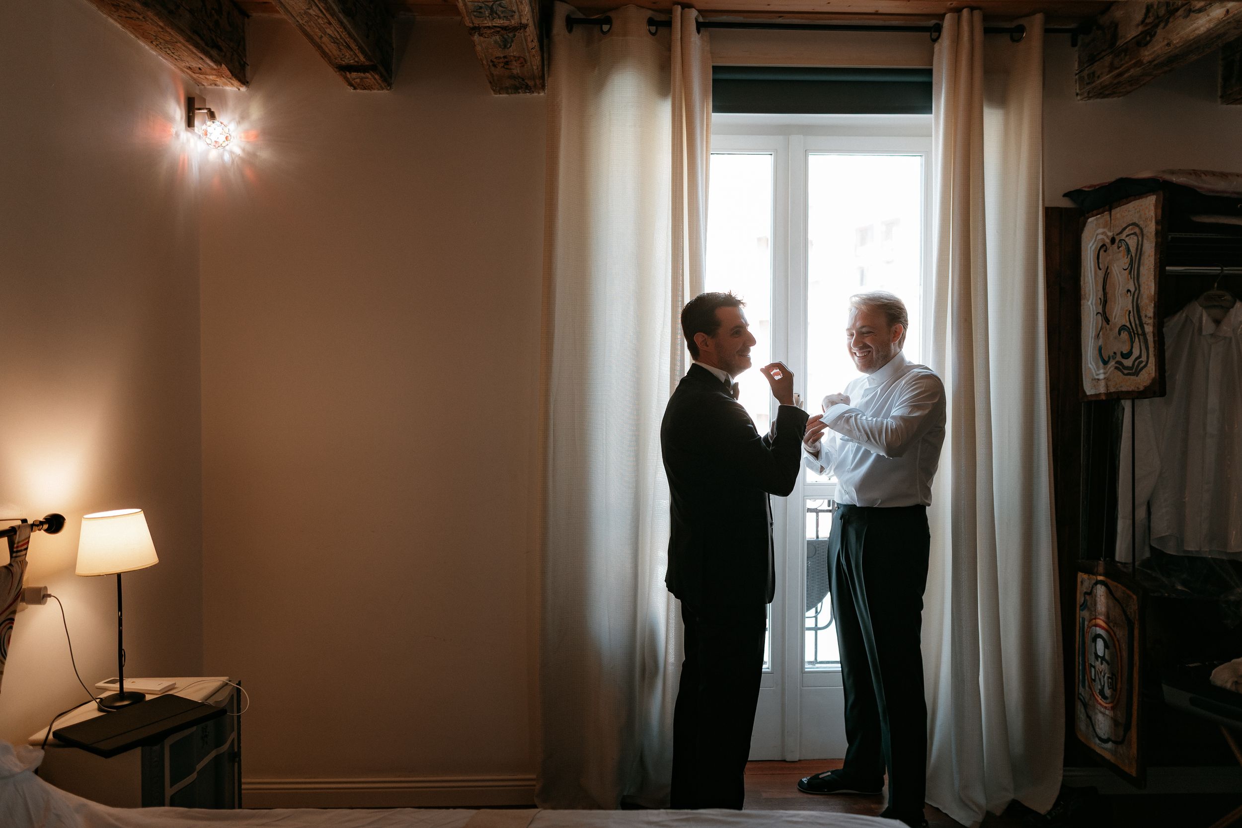 Two people stand in silhouette near a bright window in a cozy room with warm lighting and curtains.