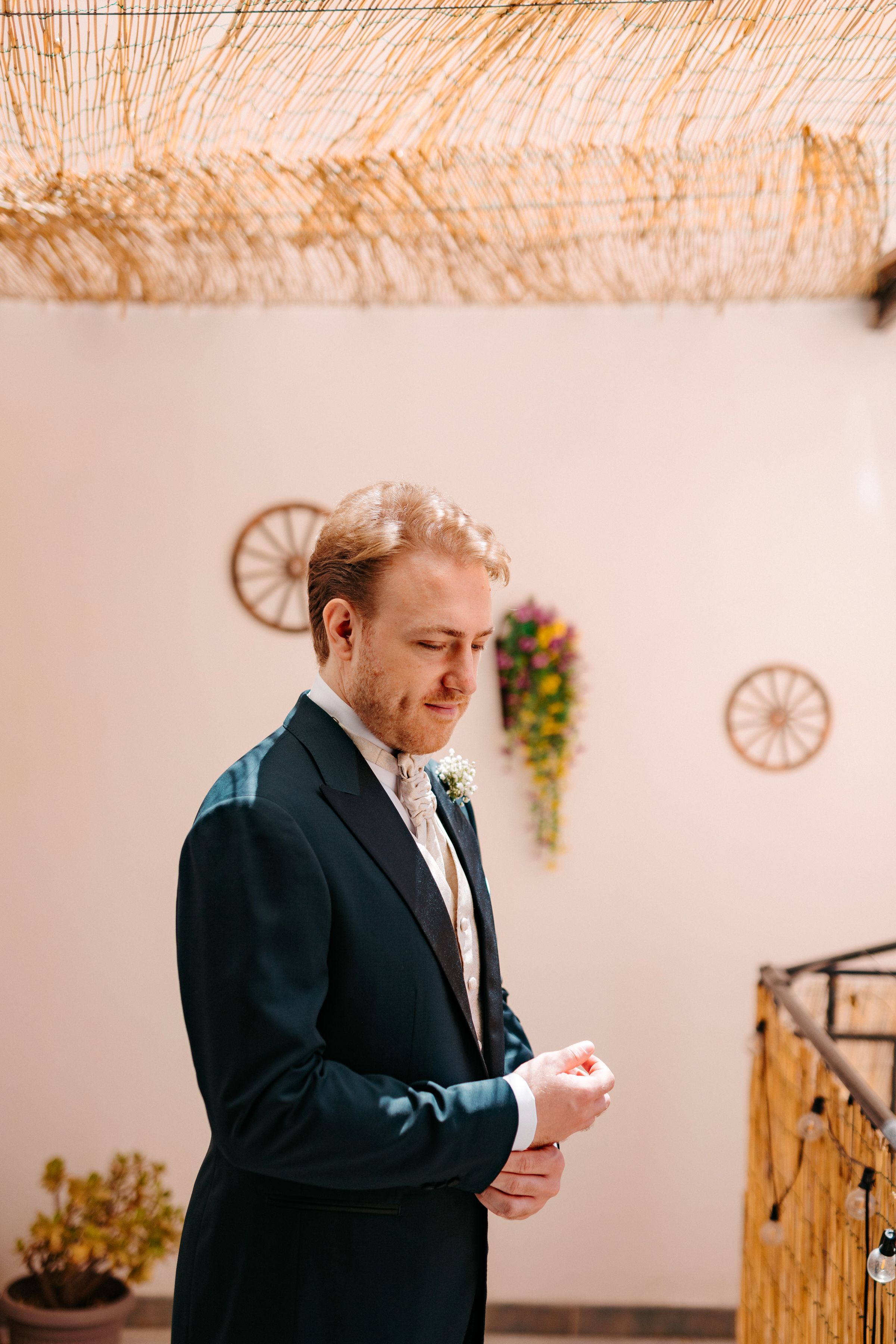 A person in a dark suit and tie looks down while standing in a rustic room with wagon wheel wall decorations.