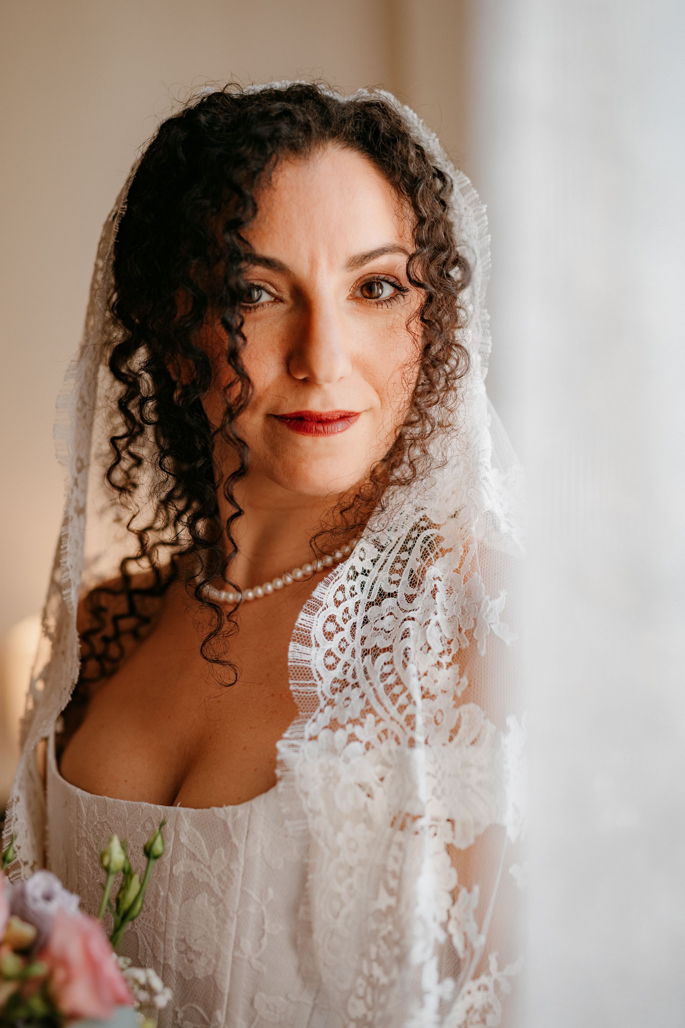 Close-up portraits of someone wearing a white lace wedding dress with curly hair and pearl necklace in warm lighting.