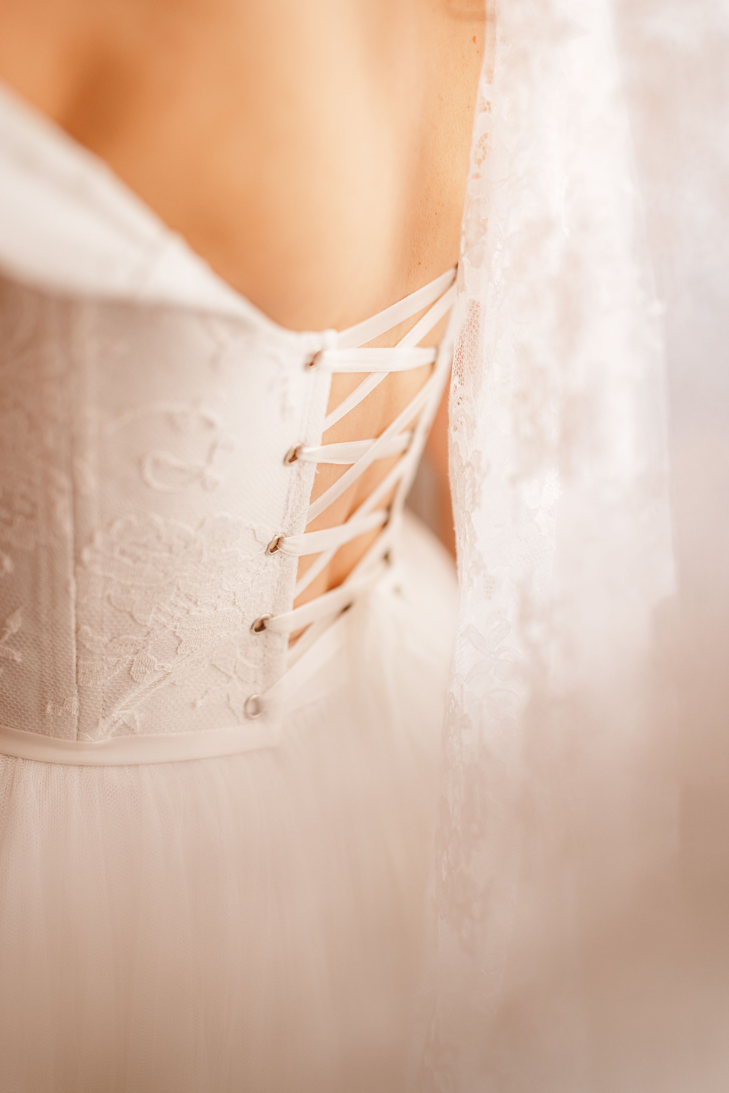 Close-up details of white corset lacing with delicate satin ribbons against a soft blurred background.