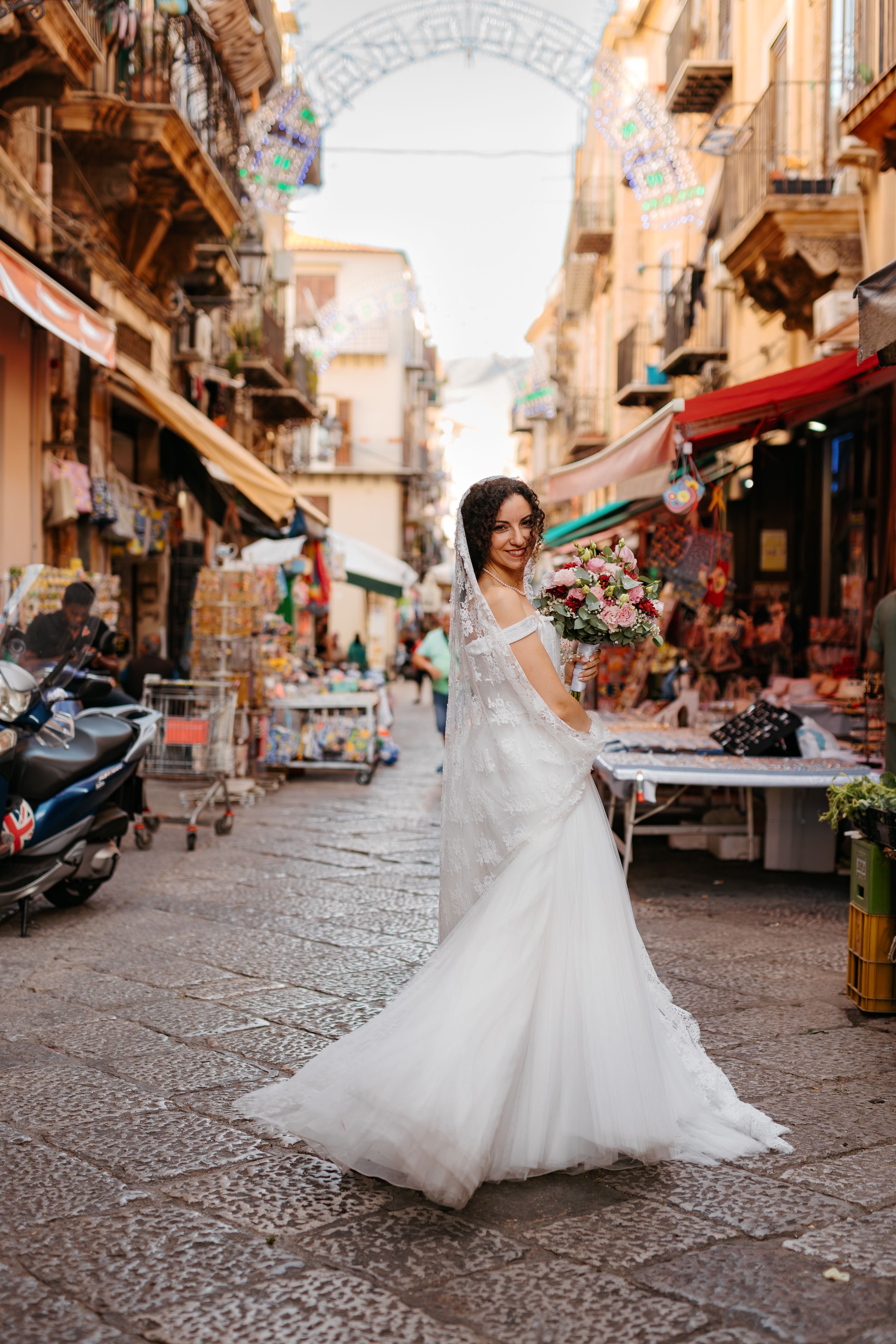 A bride in a flowing white gown twirls gracefully on a charming cobblestone street in an old Italian neighborhood.