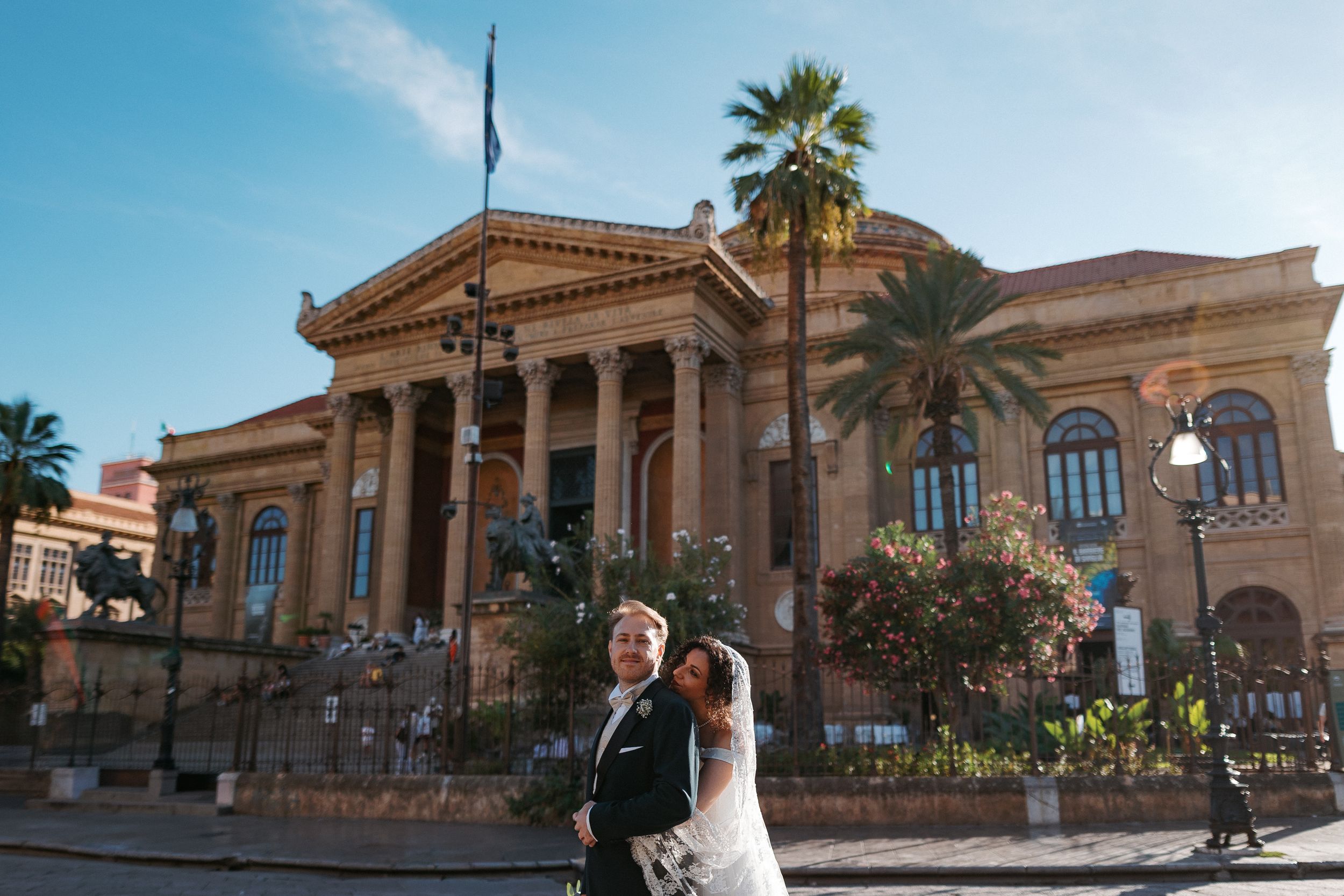 Historic Teatro Massimo opera house in Palermo, Sicily with palm trees and classical architecture under blue sky.