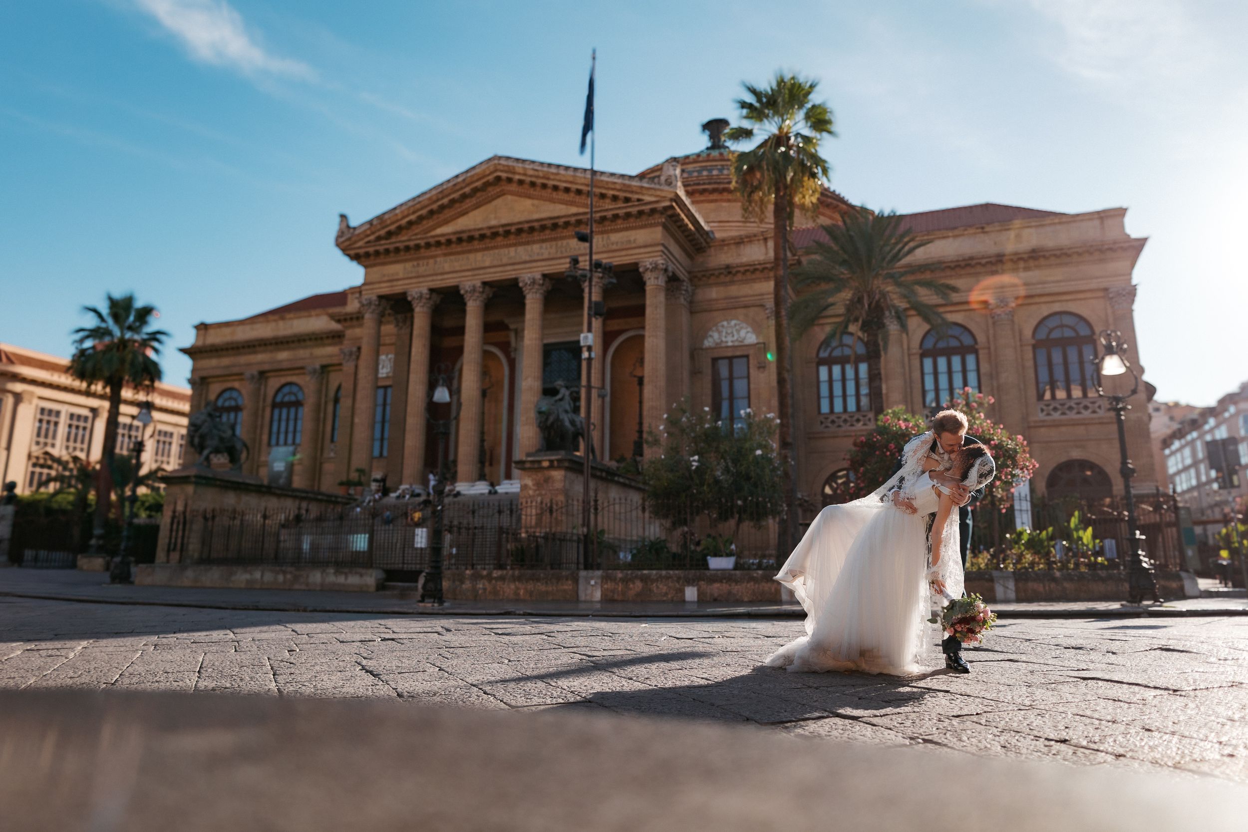 A couple in wedding attire poses in front of the historic Teatro Massimo opera house in Palermo, Sicily.