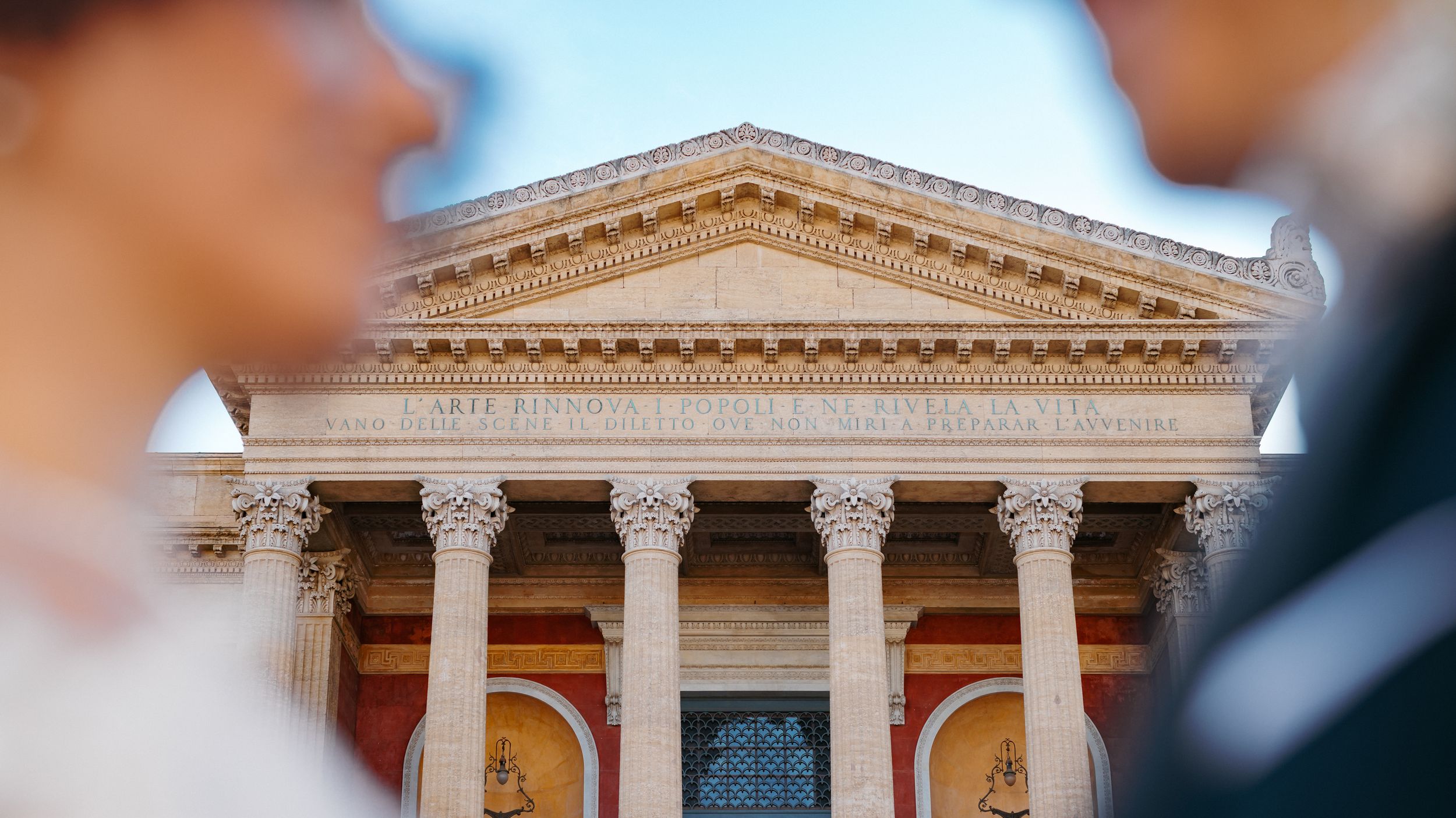 Majestic white marble courthouse building with classical Greek columns and ornate architectural details stands against blue sky.