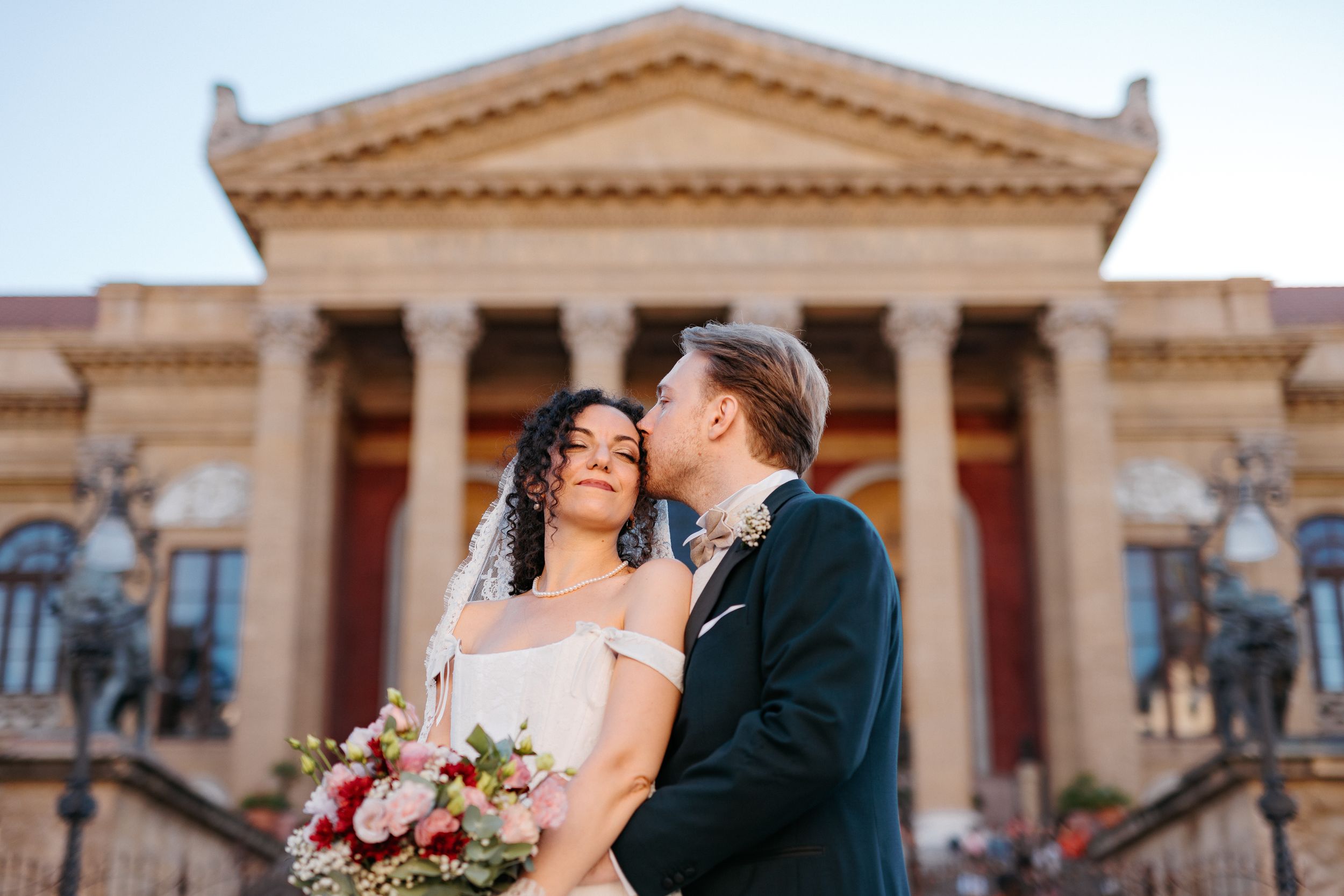 A romantic wedding couple shares an intimate moment in front of the Teatro Massimo opera house in Palermo, Italy.