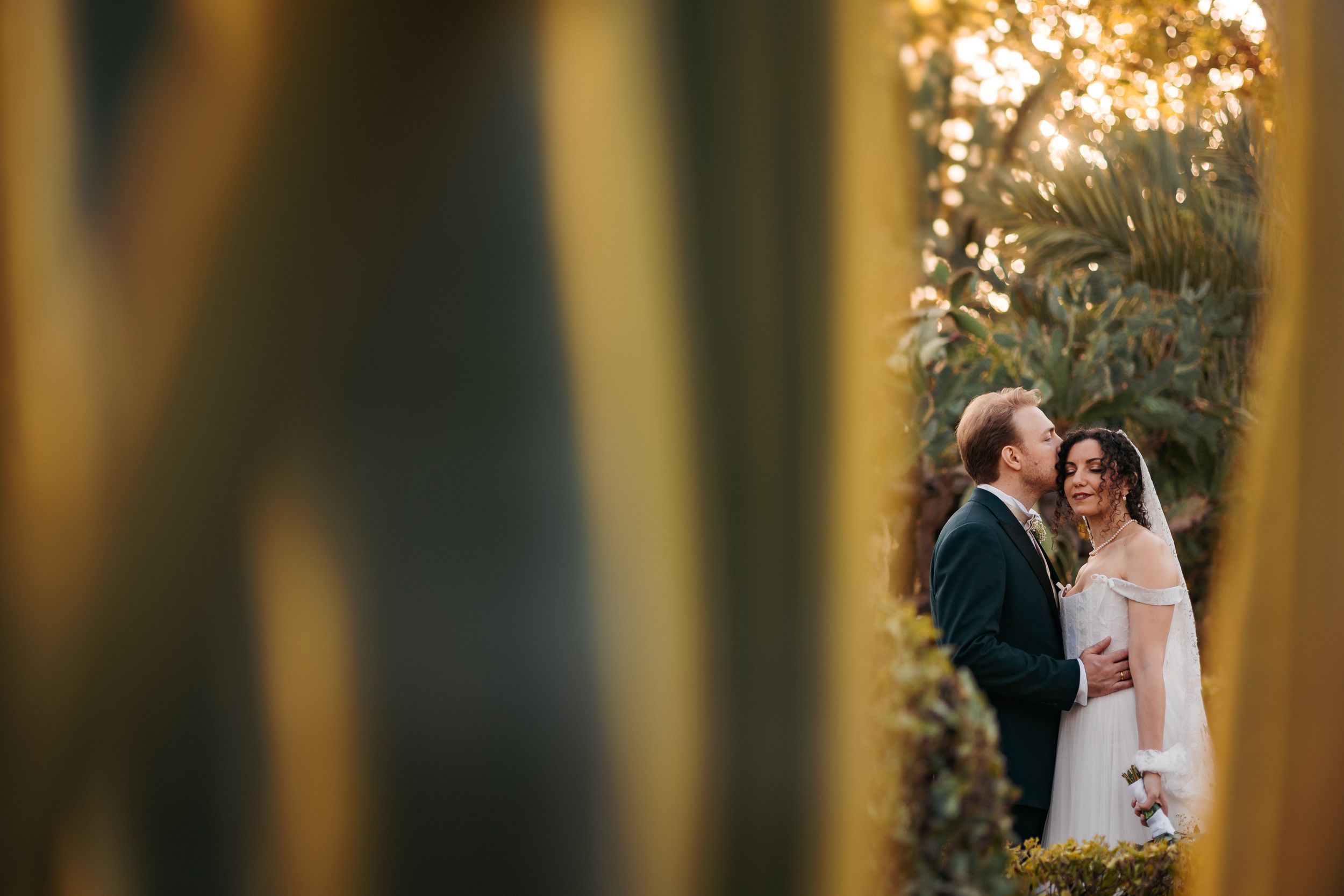 A romantic wedding couple shares a tender moment outdoors during golden hour with glowing bokeh lights in the background.