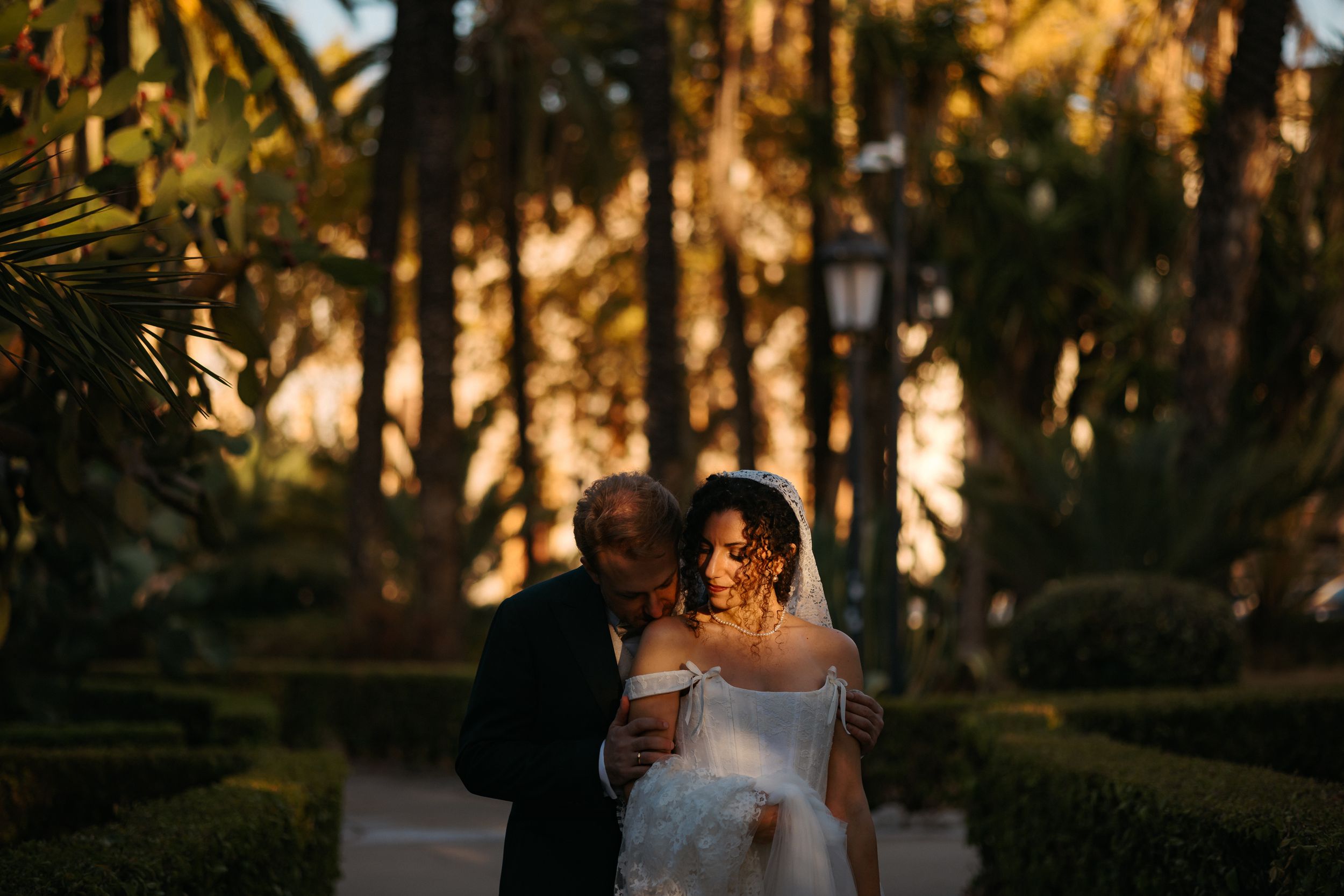 A couple walks together through a garden path at sunset with golden light filtering through trees.