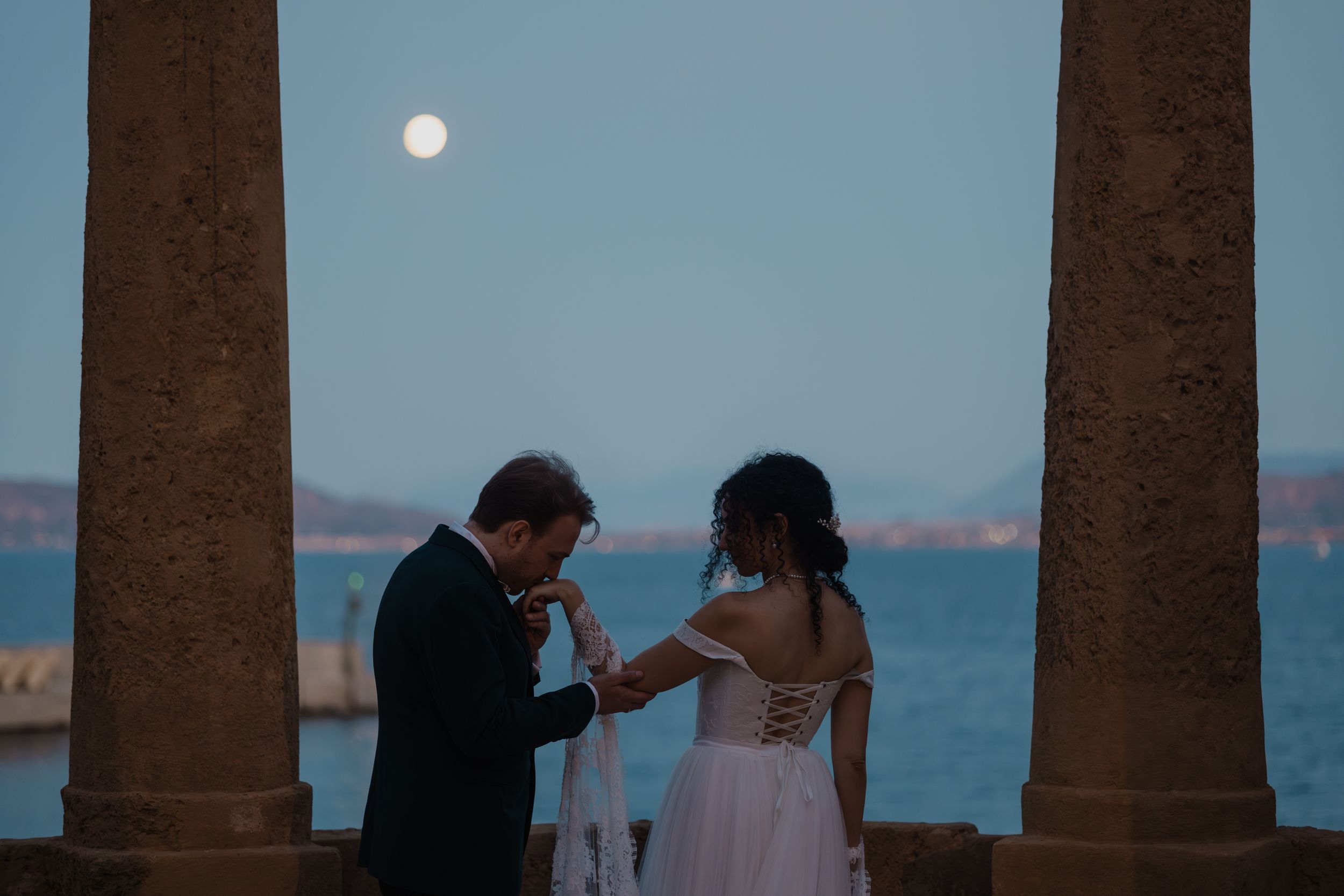 Couple dancing under stone pillars at sunset with ocean view in romantic outdoor setting.