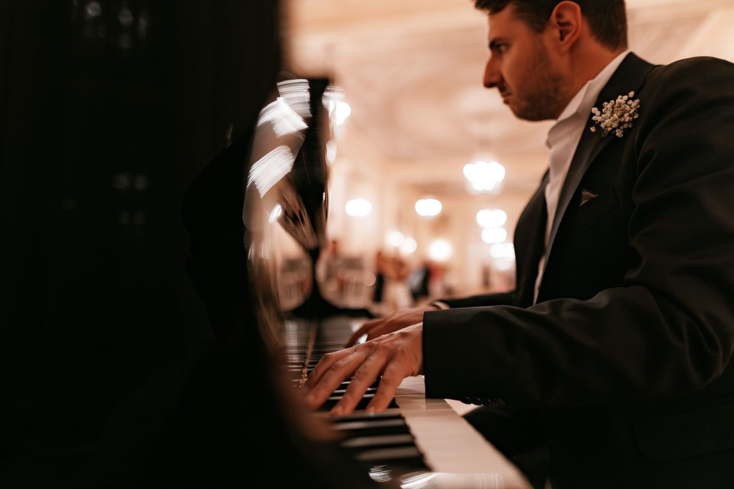 Pianist in a black suit performs at an elegant evening event with soft bokeh lights in the background.