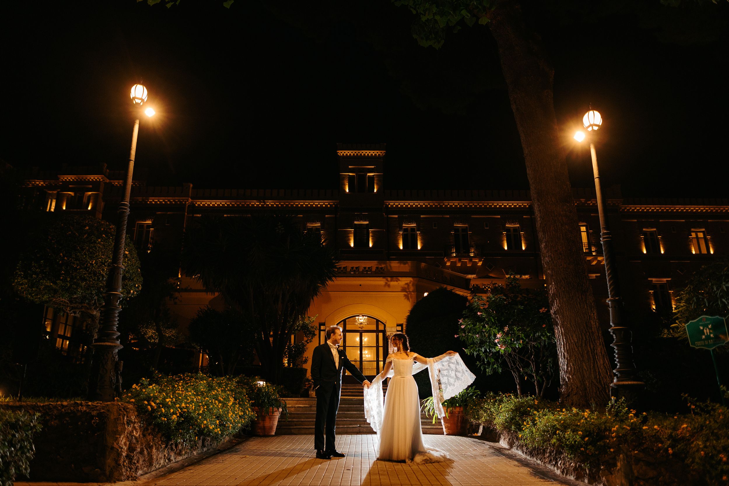 Romantic outdoor evening wedding venue illuminated by glowing string lights and lanterns.