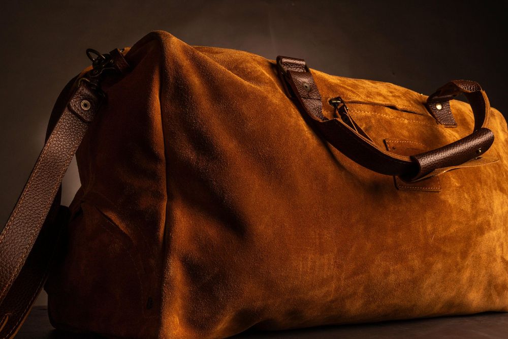 Bolso de viaje de cuero gamuzado marrón con correas de cuero fotografiado con iluminación dramática.