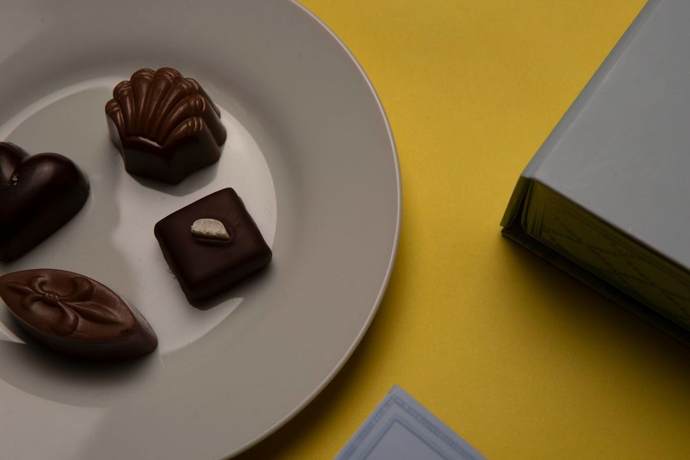 Dark chocolate truffles and candies arranged on white plates against a bright yellow background.