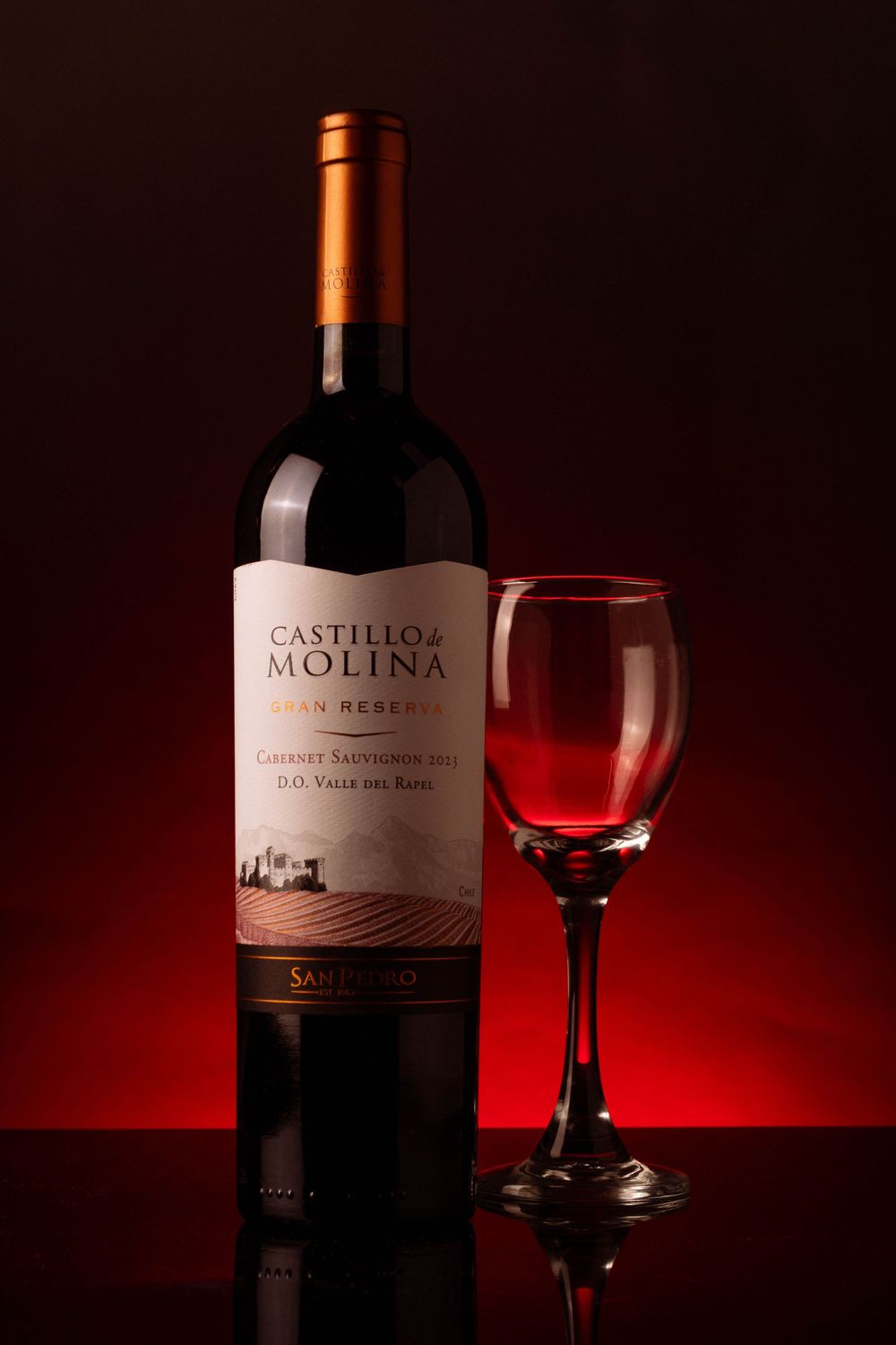 Botella de vino tinto Castillo de Molina con copa llena sobre fondo rojo oscuro.
