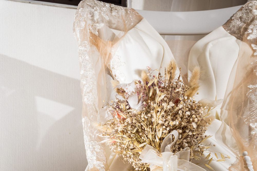 Escote de vestido de novia con encaje delicado y ramo de flores secas.