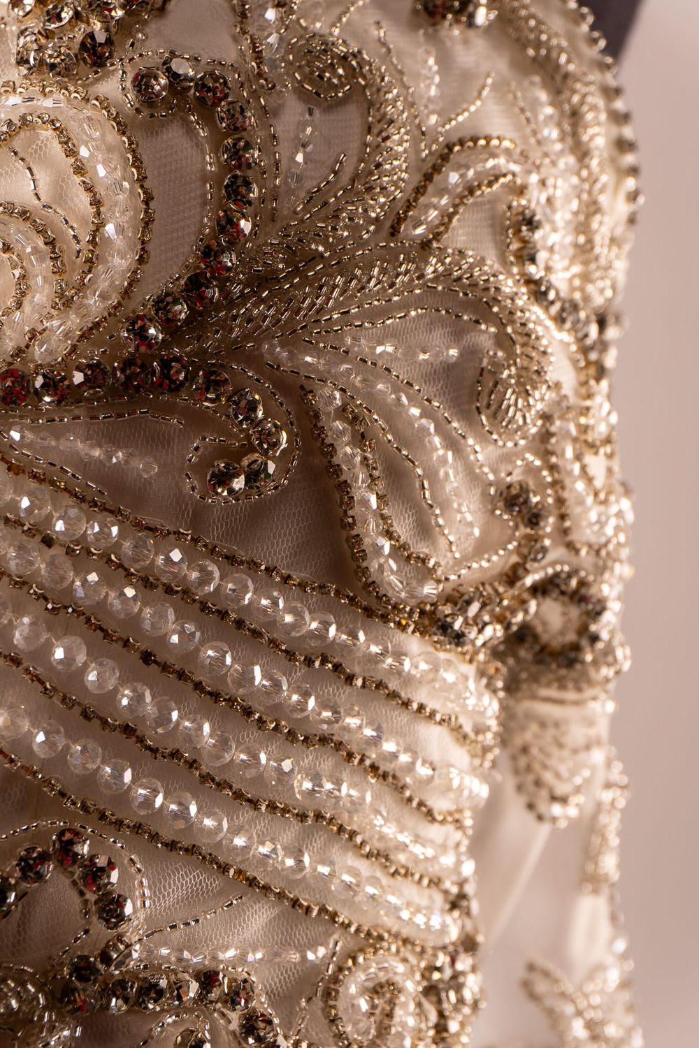 Detalle intrincado de bordados y lentejuelas en tela de vestido formal color champaña.
