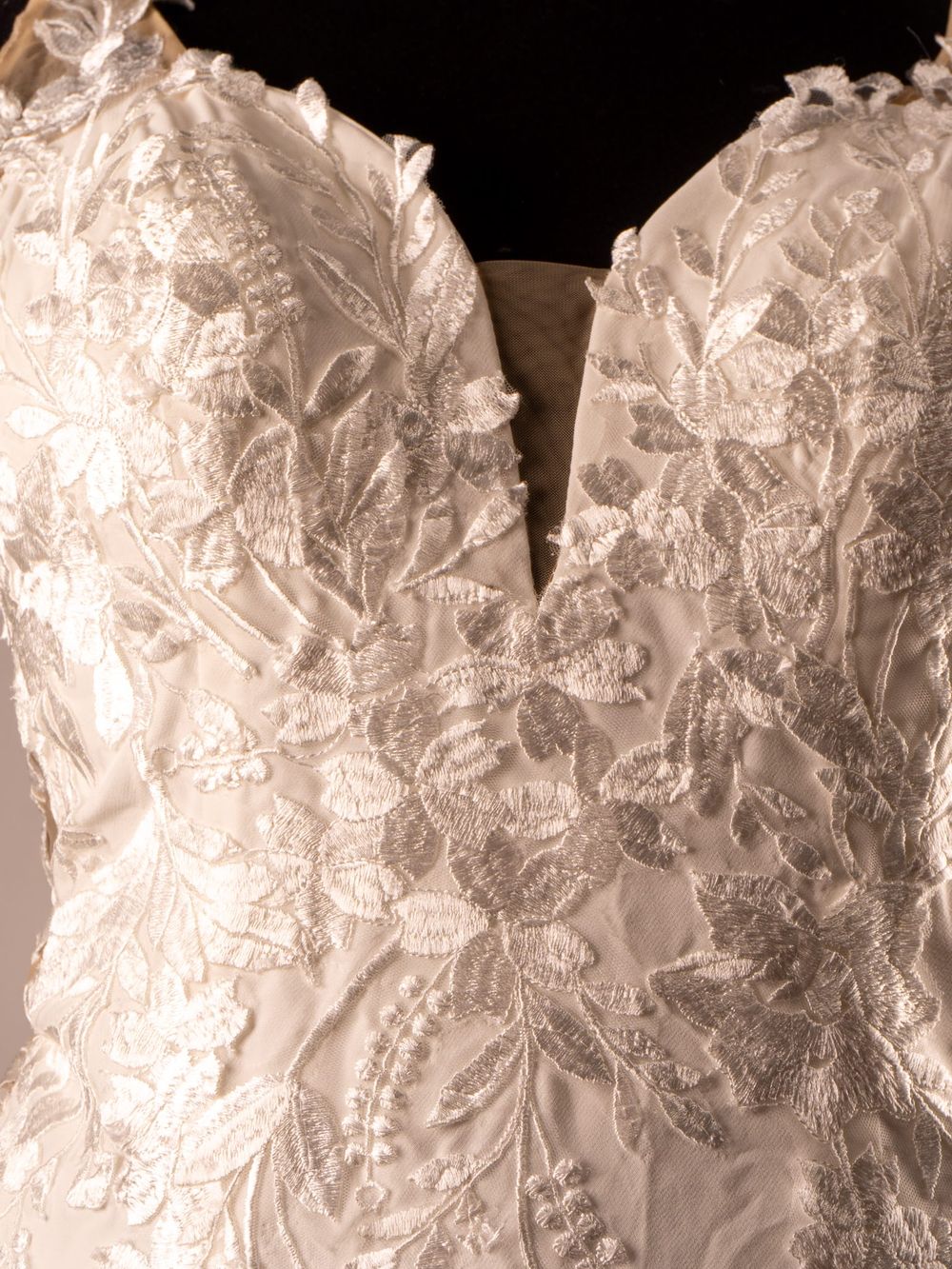 Primer plano de vestido de novia blanco mostrando patrón detallado de bordado en encaje.