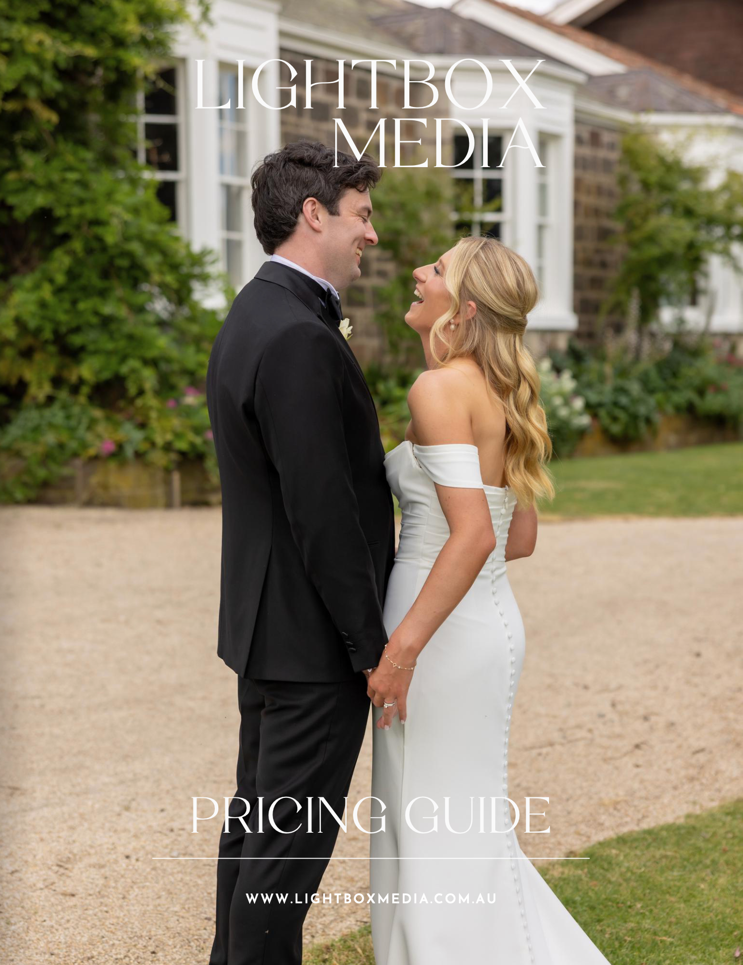 Couple in wedding attire walking together on a sandy beach path near a white building on their special day.