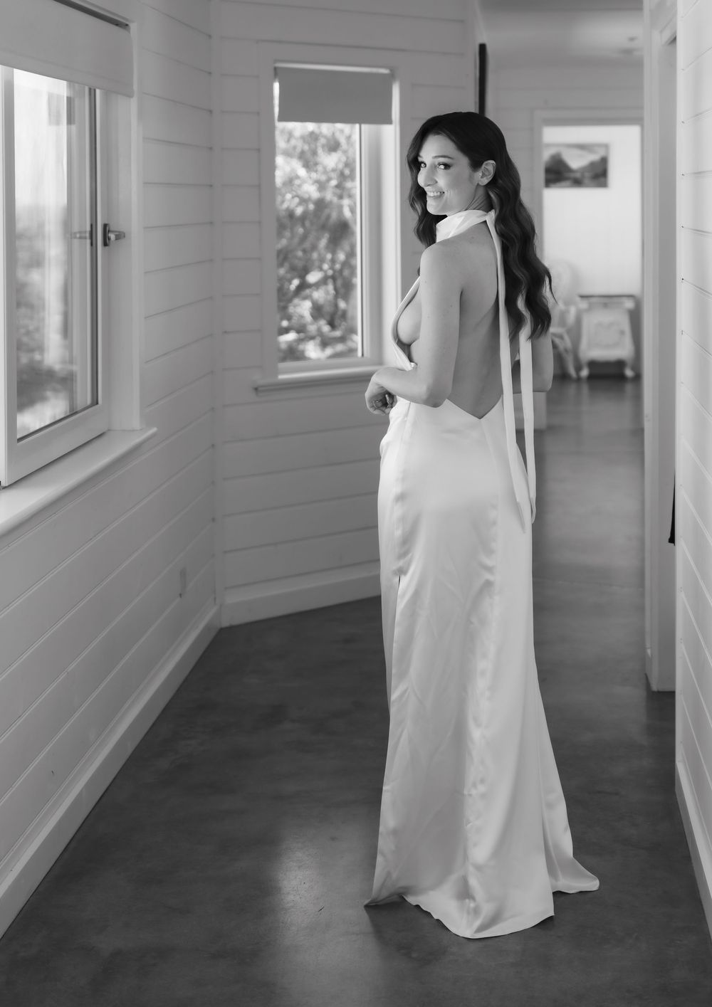 A figure in a flowing white dress moves gracefully through a minimalist gallery hallway with white walls.