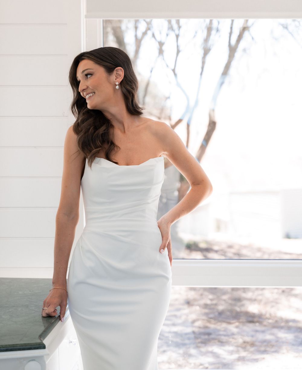 Elegant strapless white wedding dress shown in natural lighting by a window.