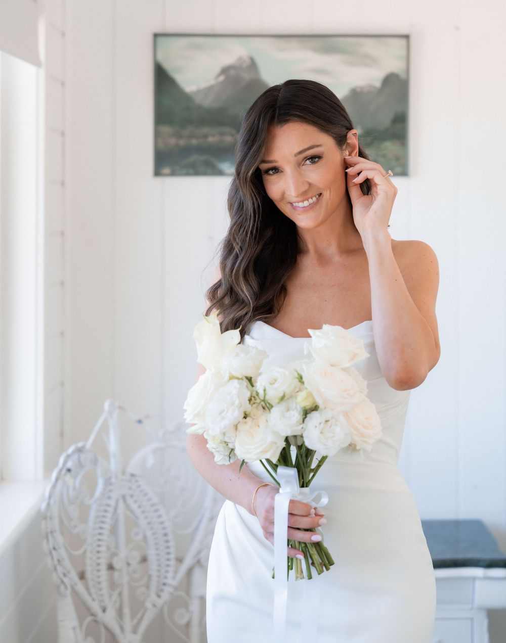 A bride in a white dress holds a bouquet of white flowers while posing in an elegant indoor setting.