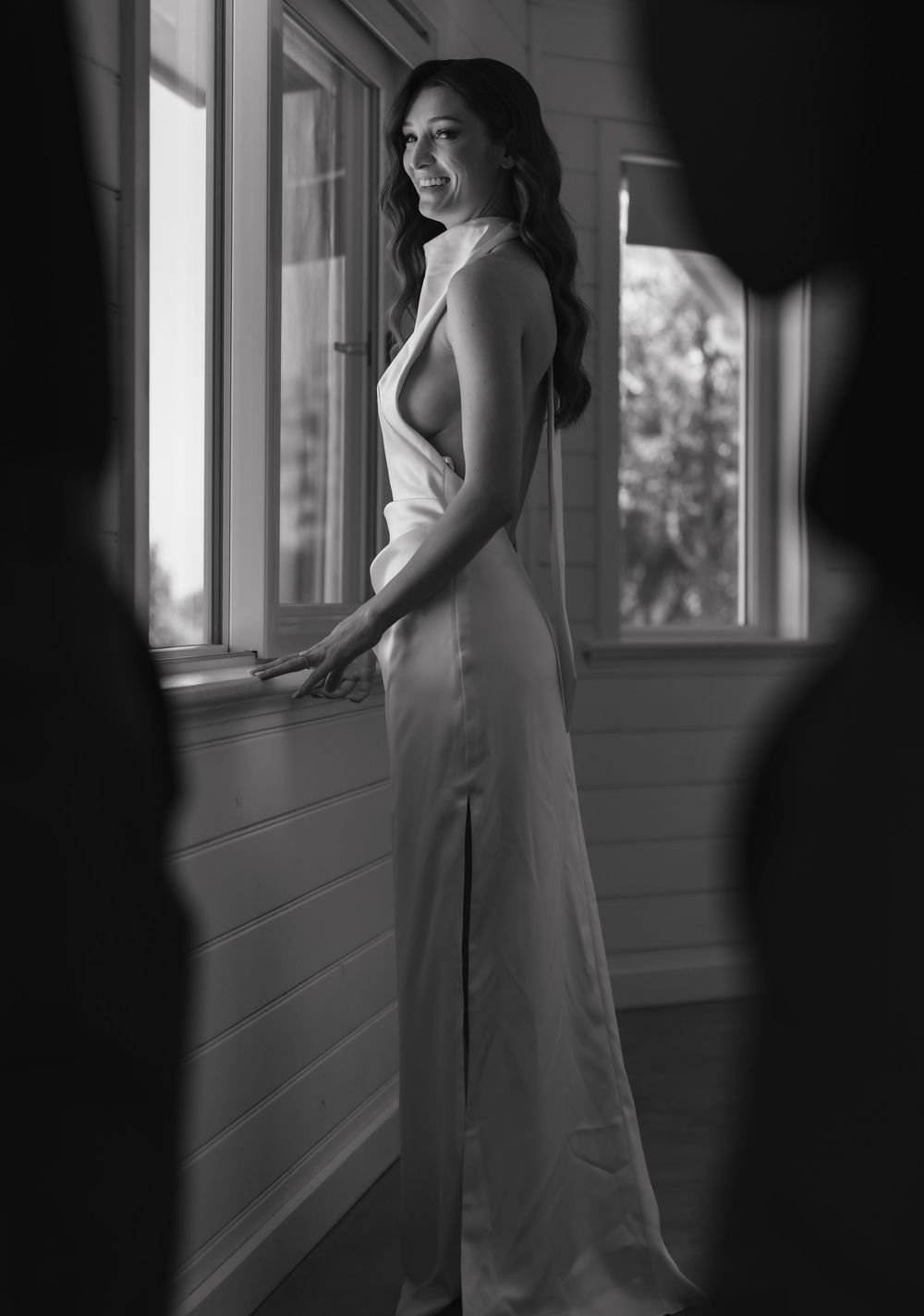 A series of black and white photos showing a bride in a white dress posing near sunlit windows in a hallway.