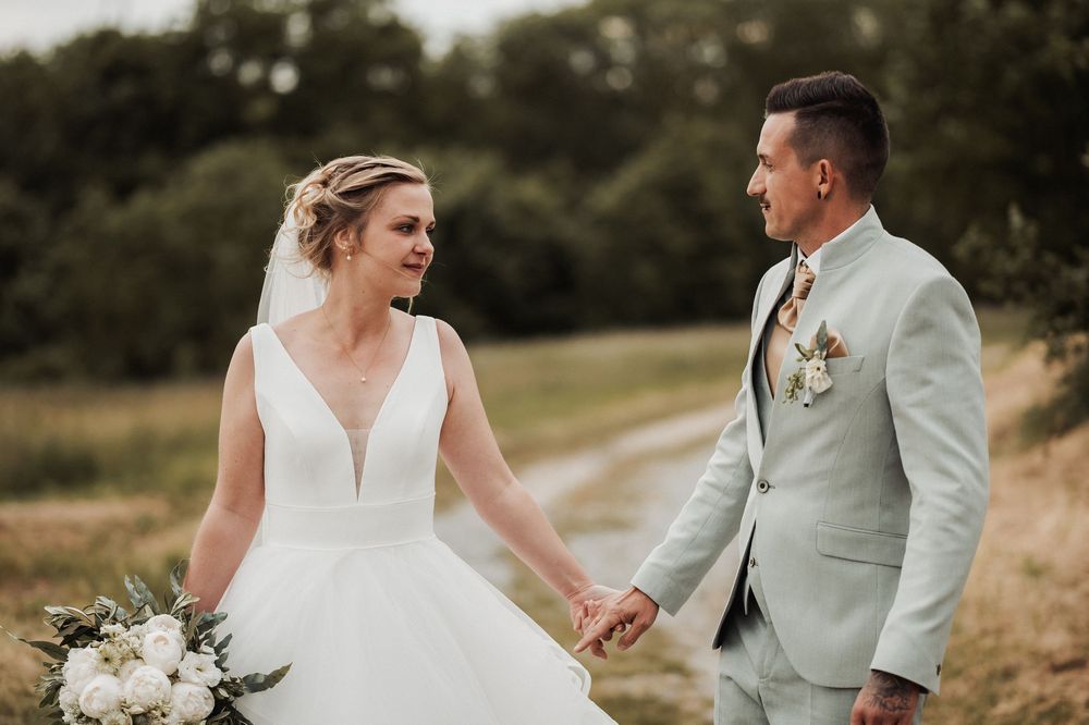A couple in wedding attire shares a romantic moment in a golden field during sunset.